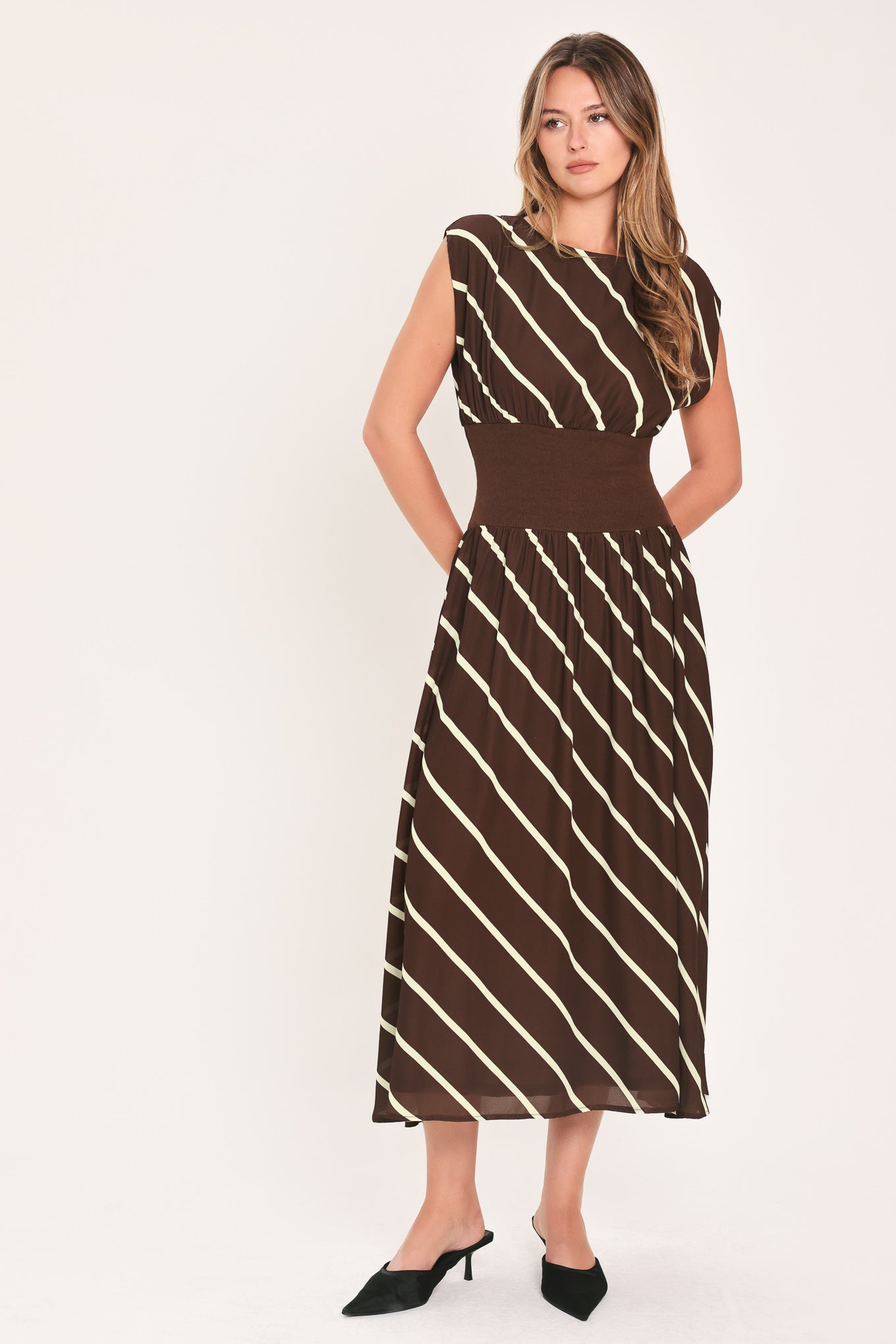 A woman modeling a sleeveless midi dress with a brown and cream diagonal striped pattern, featuring a defined waistband | Flying Tomato
