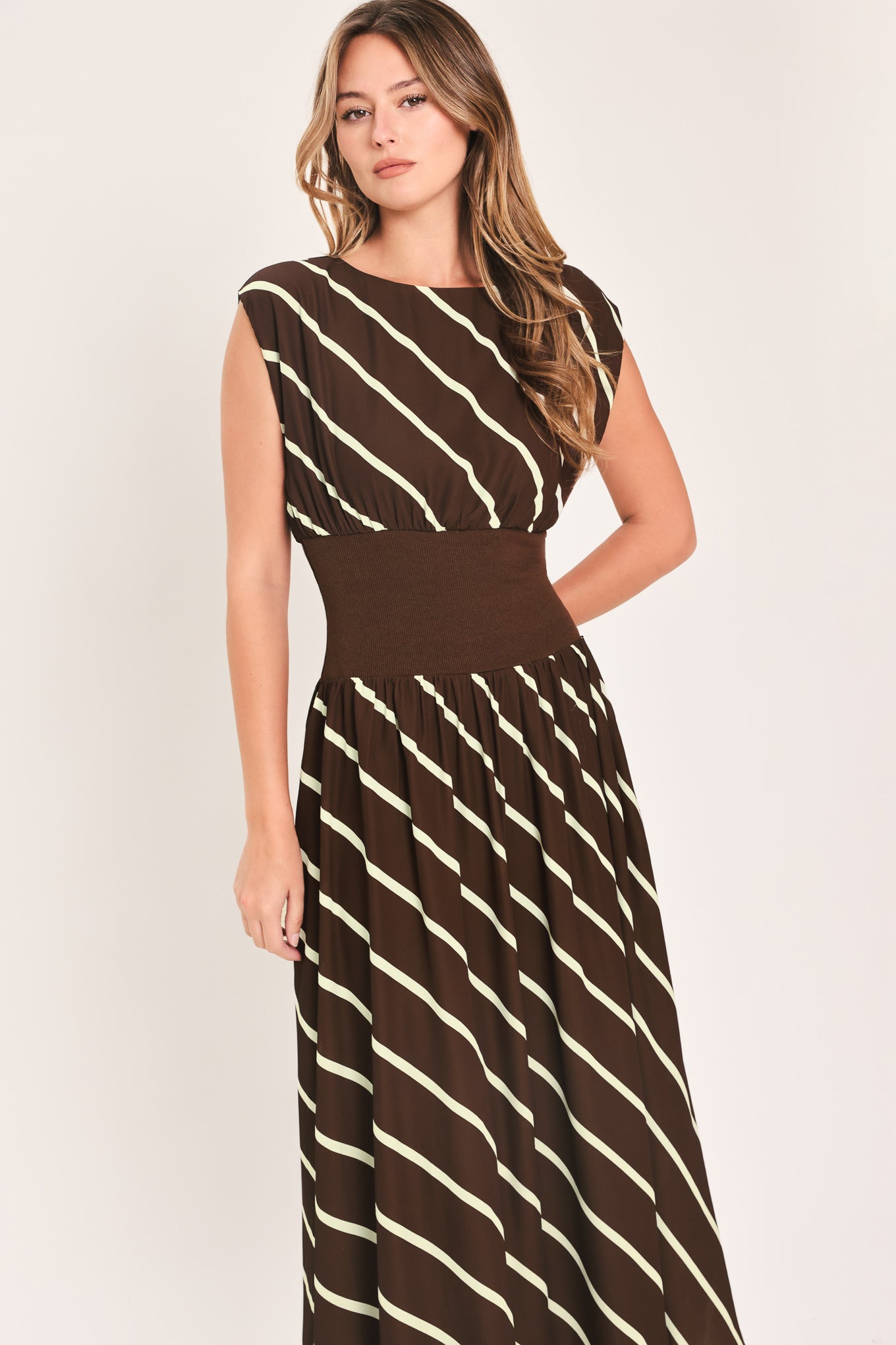 A woman modeling a sleeveless midi dress with a brown and cream diagonal striped pattern, featuring a defined waistband | Flying Tomato