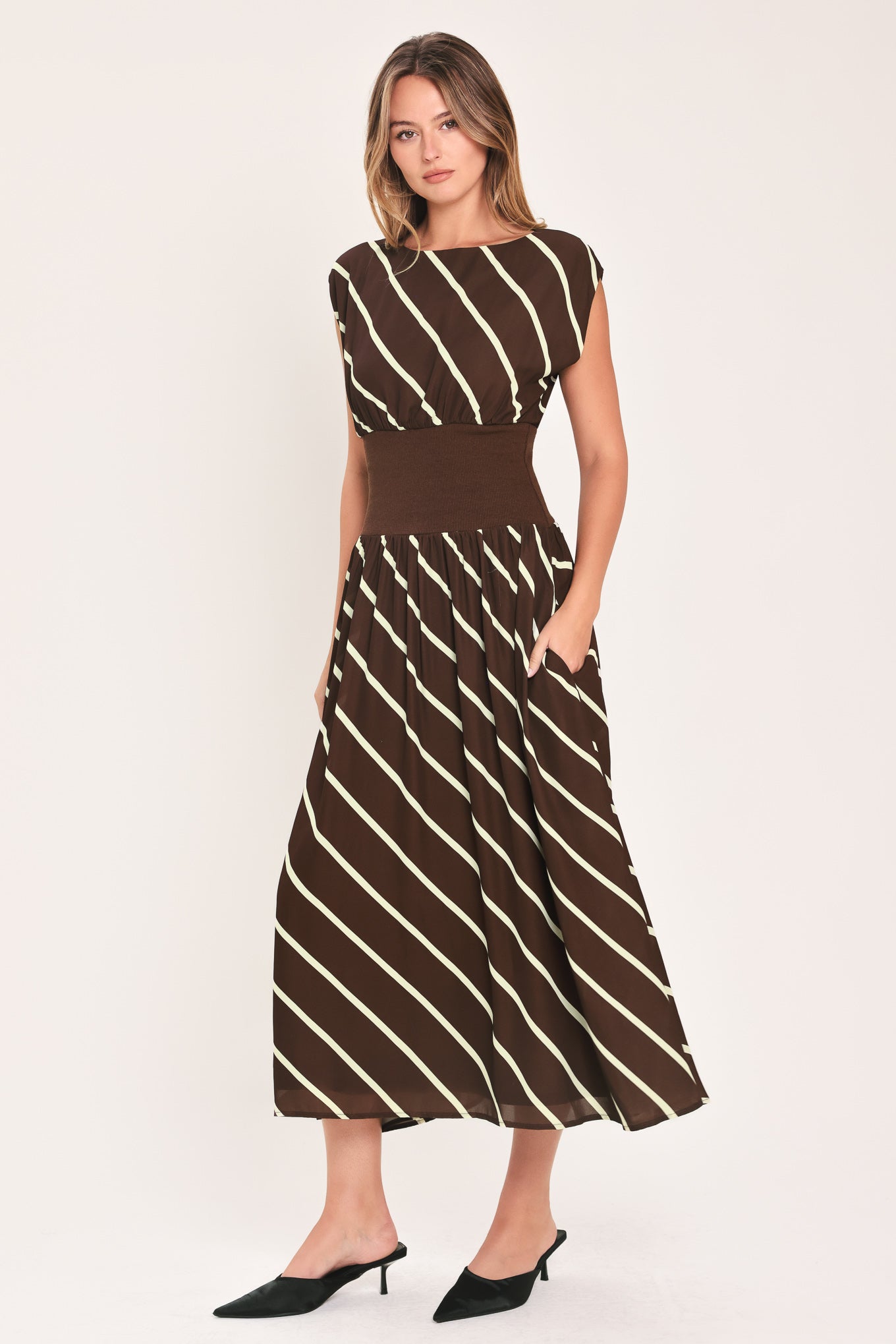 A woman modeling a sleeveless midi dress with a brown and cream diagonal striped pattern, featuring a defined waistband | Flying Tomato