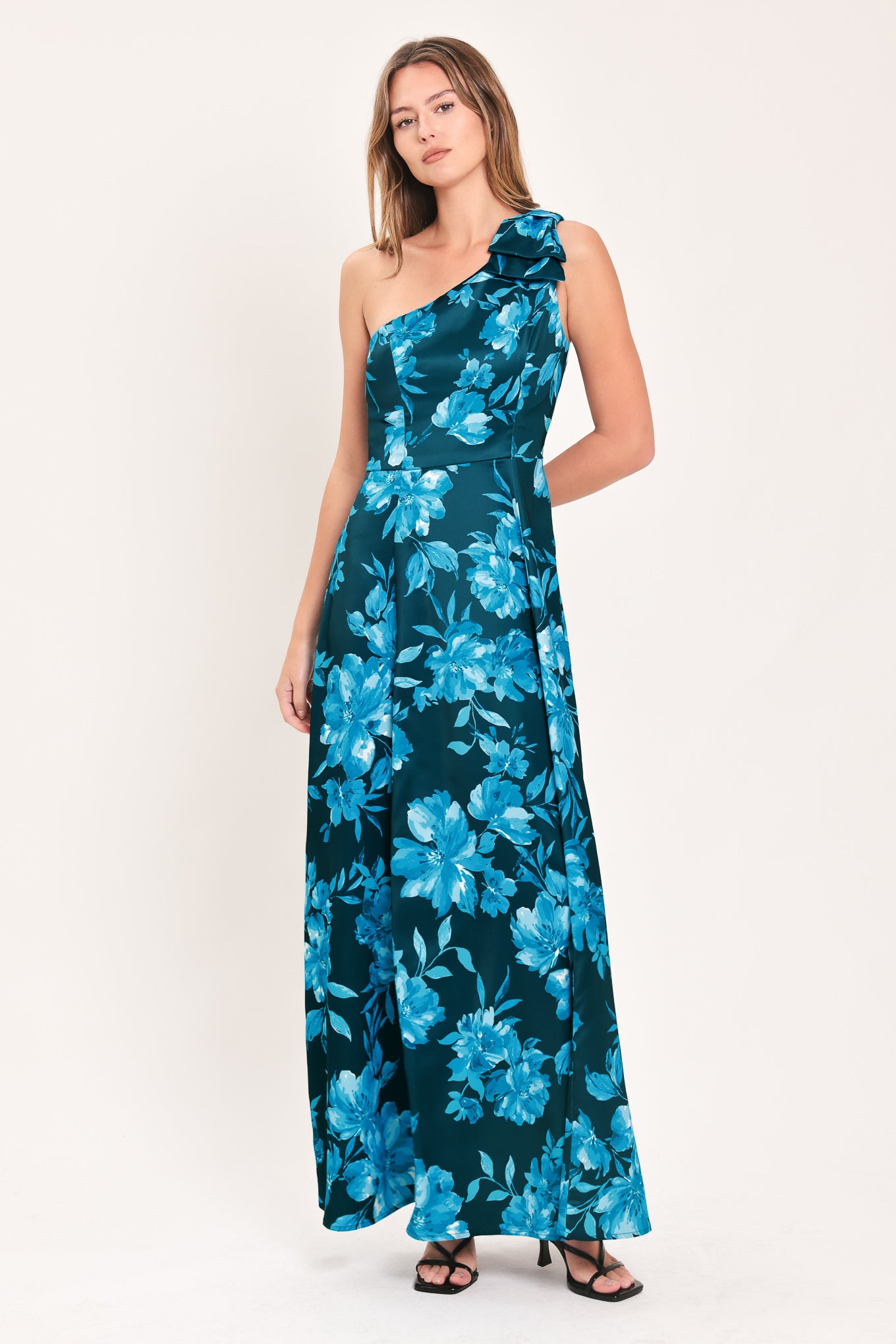 A woman modeling a one-shoulder maxi dress with a vibrant blue floral print on a dark teal background | Flying Tomato