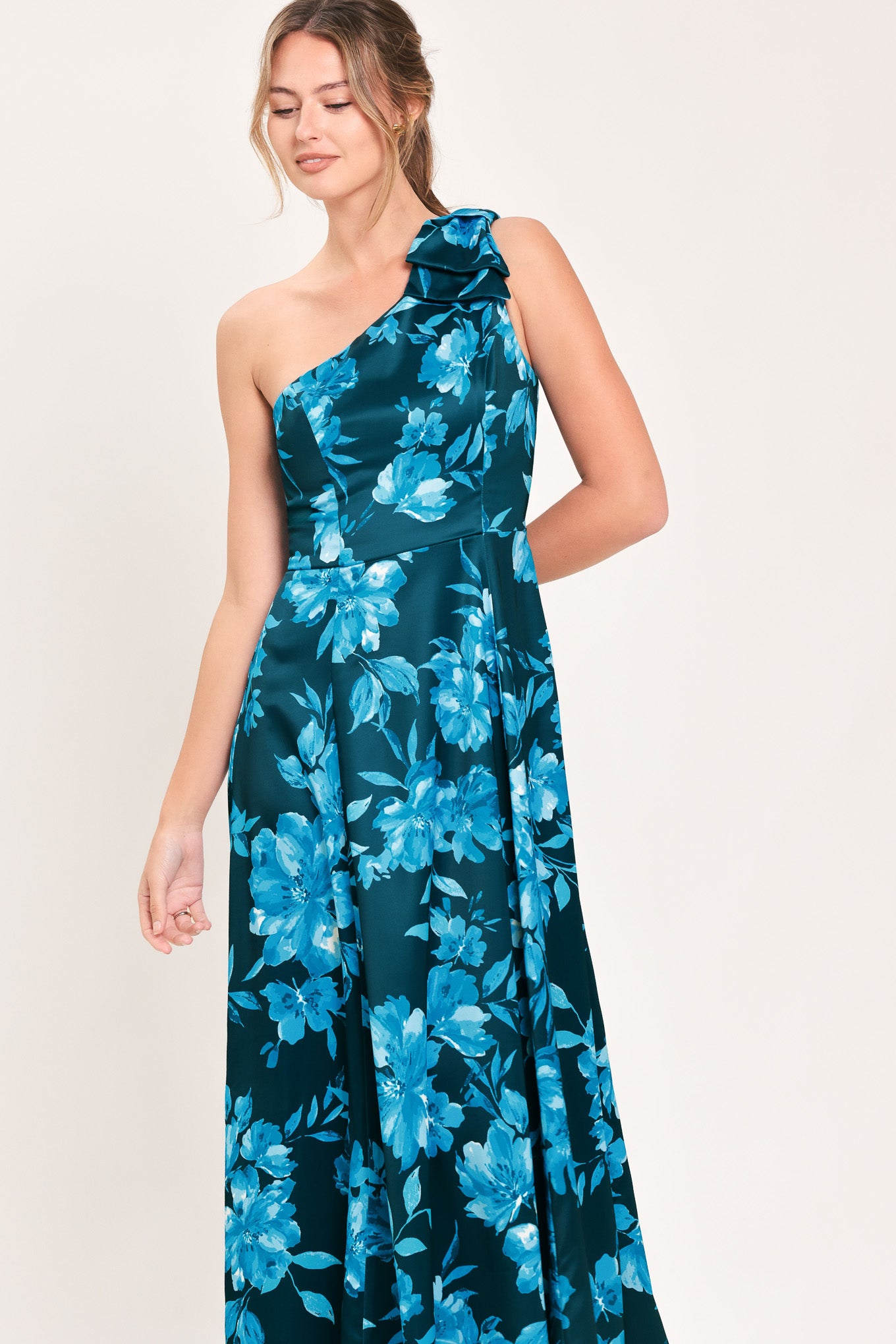 A woman modeling a one-shoulder maxi dress with a vibrant blue floral print on a dark teal background | Flying Tomato