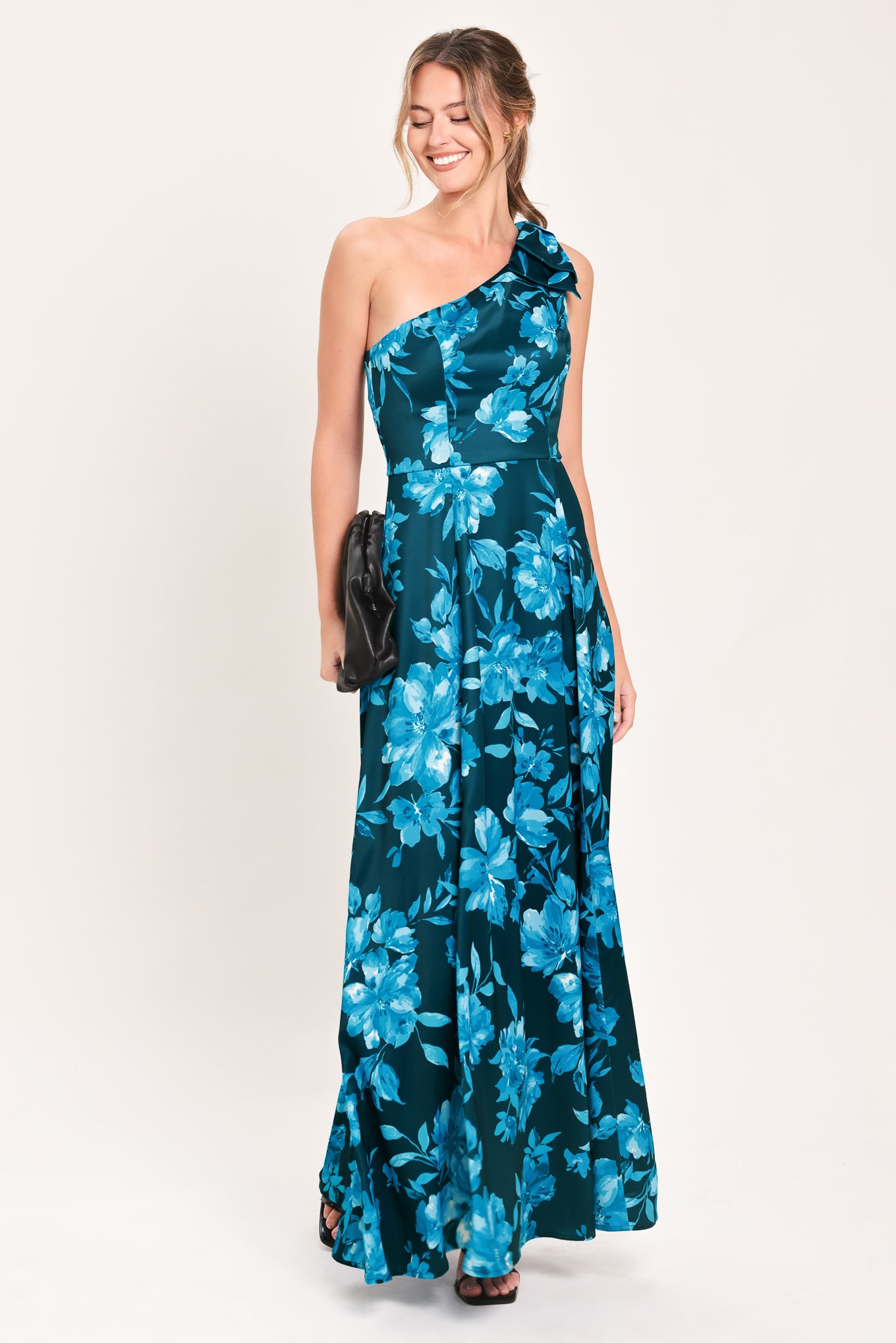 A woman modeling a one-shoulder maxi dress with a vibrant blue floral print on a dark teal background | Flying Tomato