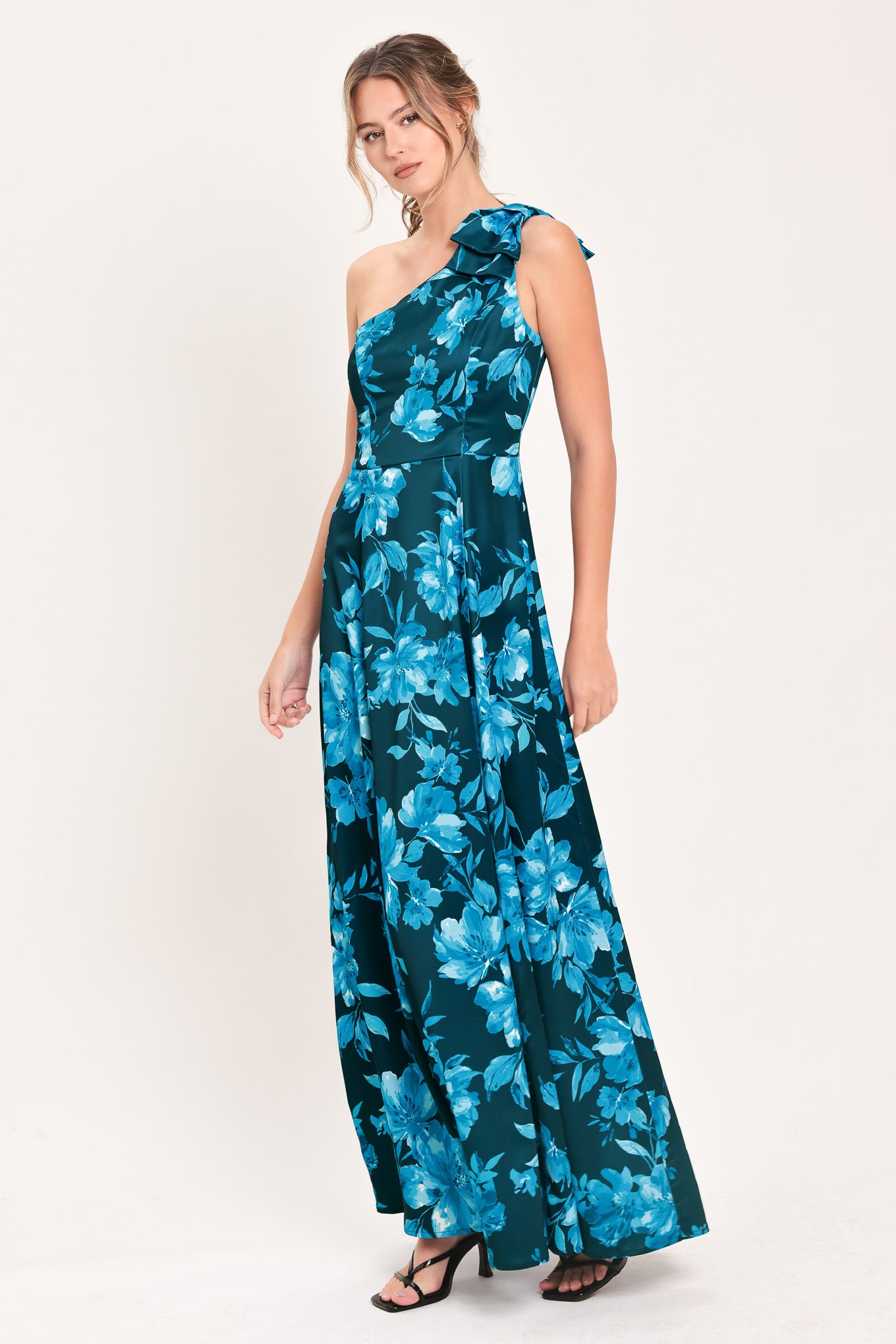 A woman modeling a one-shoulder maxi dress with a vibrant blue floral print on a dark teal background | Flying Tomato