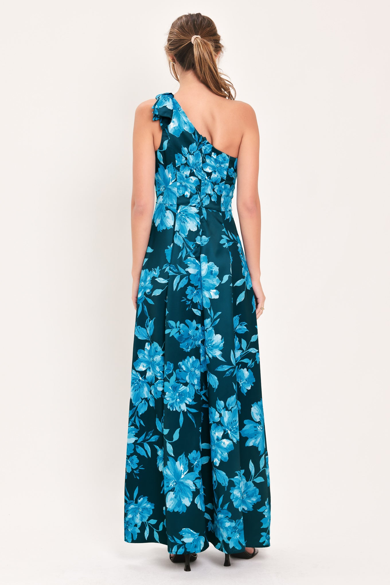 A woman modeling a one-shoulder maxi dress with a vibrant blue floral print on a dark teal background | Flying Tomato
