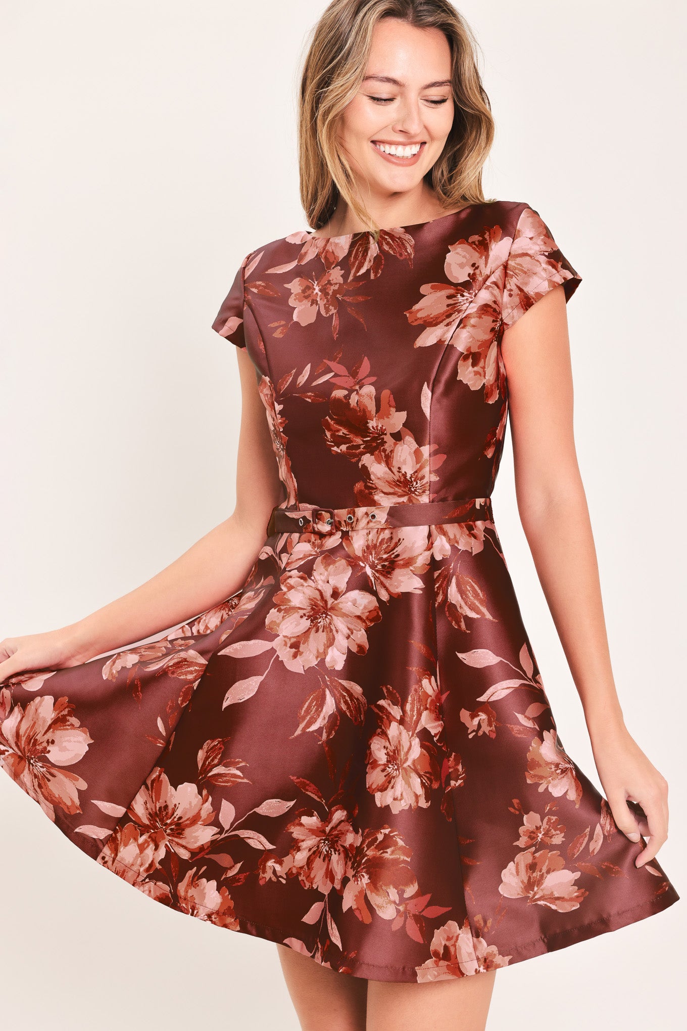 A woman modeling a short-sleeve fit-and-flare dress with a burgundy satin-like base and a pink floral pattern | Flying Tomato