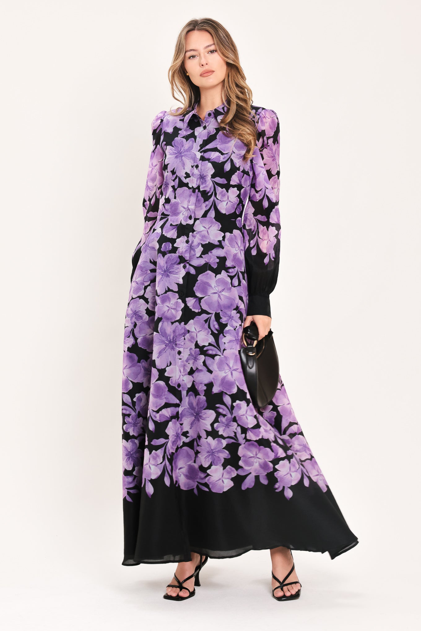 A woman modeling a long-sleeved maxi dress with a black base and a large purple floral print | Flying Tomato