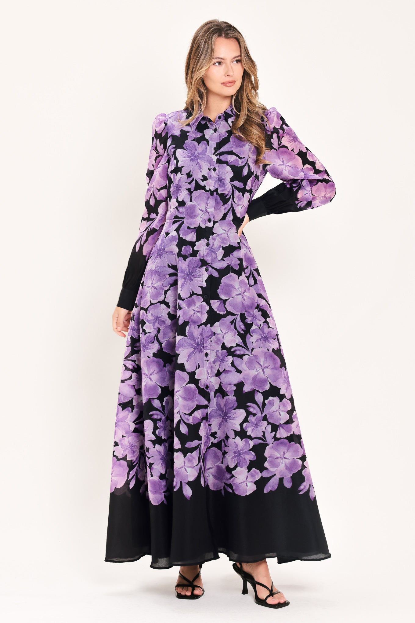 A woman modeling a long-sleeved maxi dress with a black base and a large purple floral print | Flying Tomato