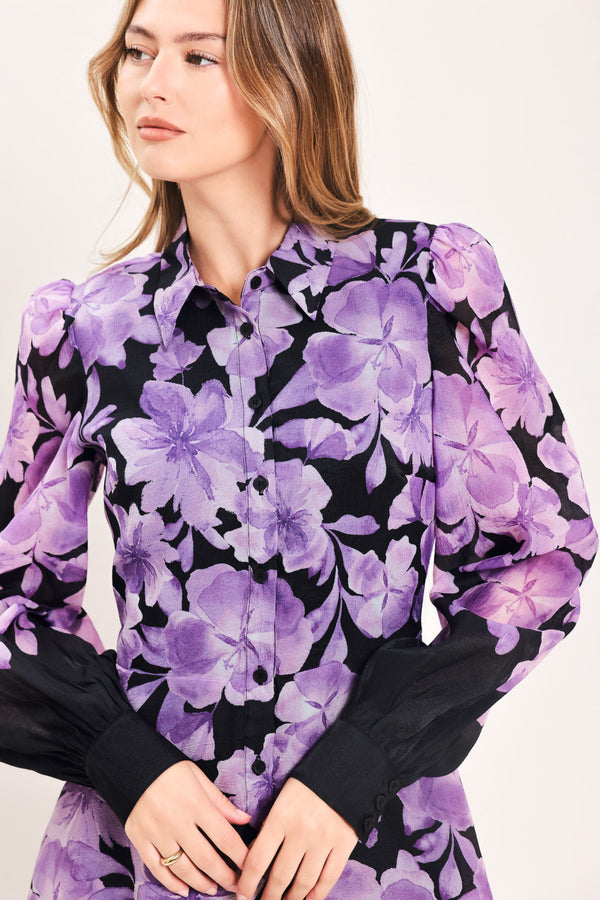 A woman modeling a long-sleeved maxi dress with a black base and a large purple floral print | Flying Tomato