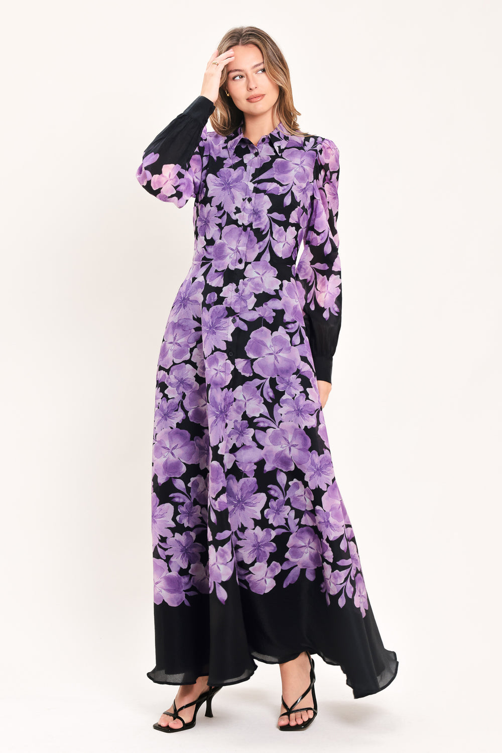 A woman modeling a long-sleeved maxi dress with a black base and a large purple floral print | Flying Tomato