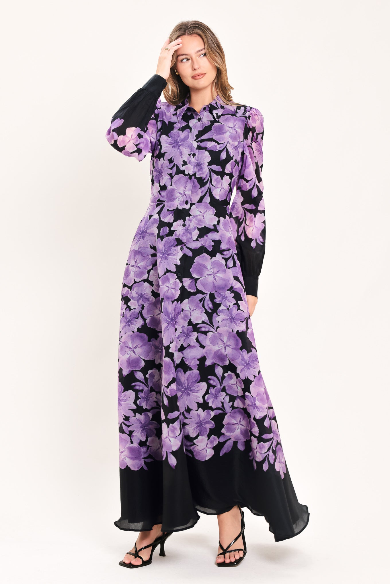 A woman modeling a long-sleeved maxi dress with a black base and a large purple floral print | Flying Tomato
