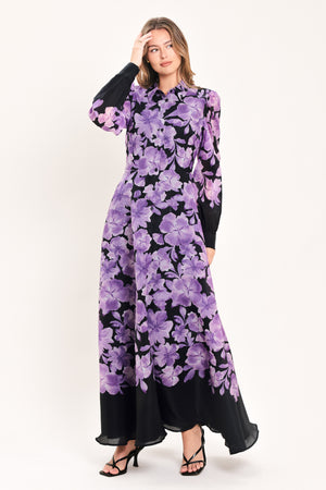 A woman modeling a long-sleeved maxi dress with a black base and a large purple floral print | Flying Tomato