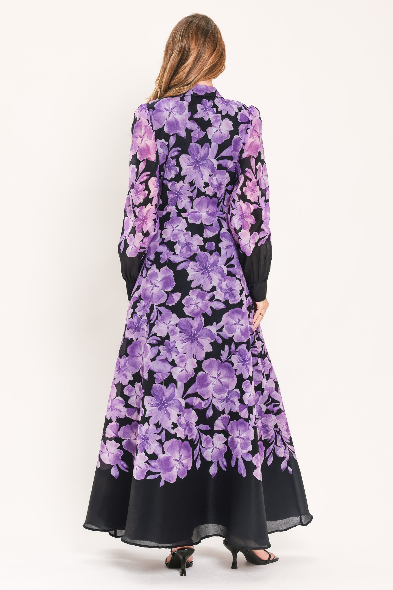 A woman modeling a long-sleeved maxi dress with a black base and a large purple floral print | Flying Tomato