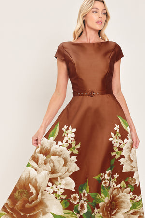 A woman models a rust satin midi dress with a floral print on the skirt, featuring white flowers, green leaves, and a matching brown belt. The dress also has cap sleeves and boatneck | Flying Tomato