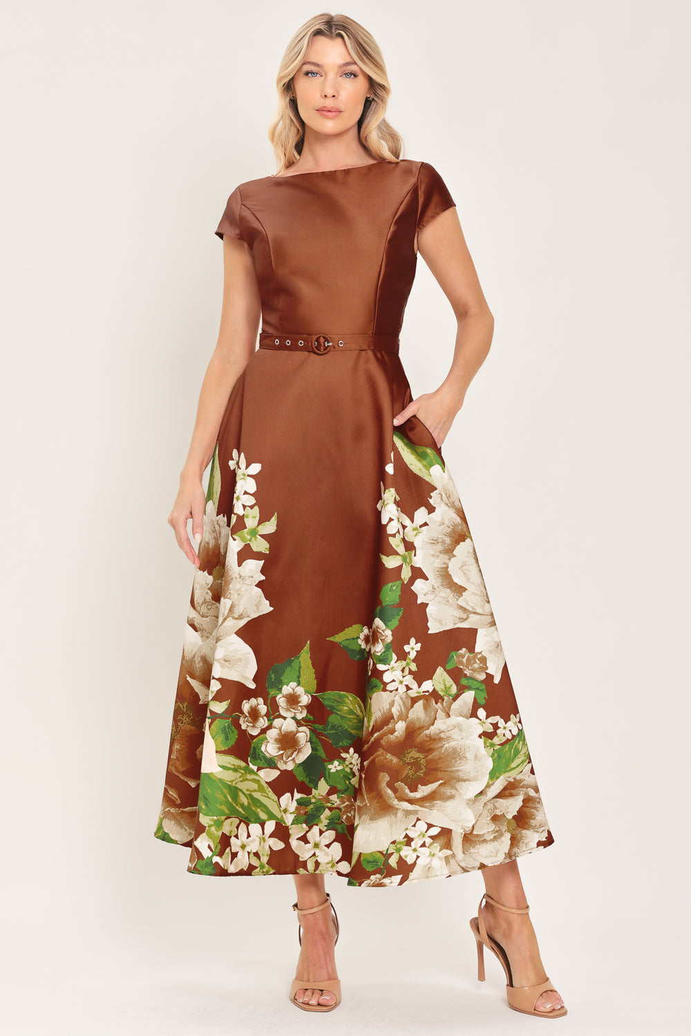 A woman models a rust satin midi dress with a floral print on the skirt, featuring white flowers, green leaves, and a matching brown belt. The dress also has cap sleeves and boatneck | Flying Tomato