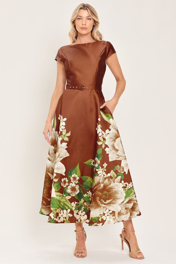 A woman models a rust satin midi dress with a floral print on the skirt, featuring white flowers, green leaves, and a matching brown belt. The dress also has cap sleeves and boatneck | Flying Tomato