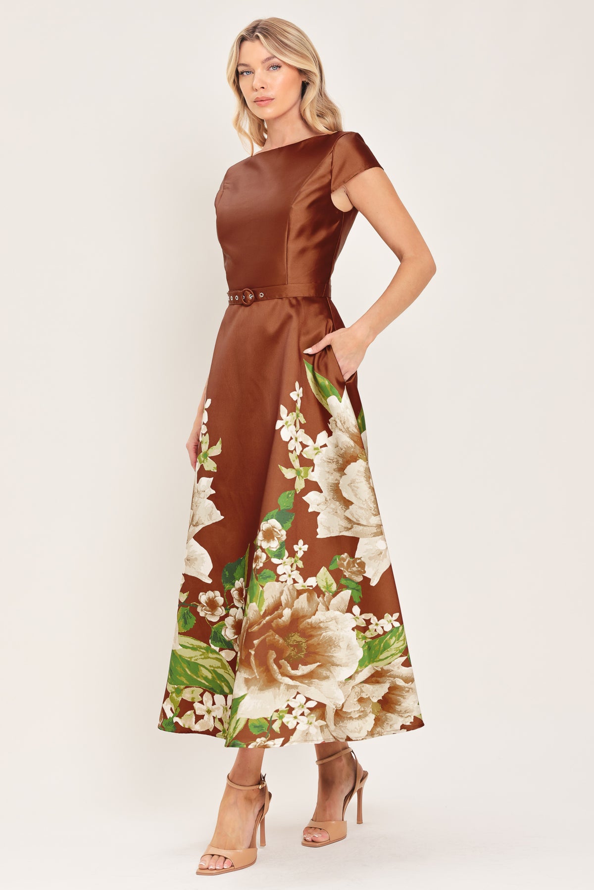 A woman models a rust satin midi dress with a floral print on the skirt, featuring white flowers, green leaves, and a matching brown belt. The dress also has cap sleeves and boatneck | Flying Tomato