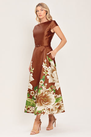 A woman models a rust satin midi dress with a floral print on the skirt, featuring white flowers, green leaves, and a matching brown belt. The dress also has cap sleeves and boatneck | Flying Tomato