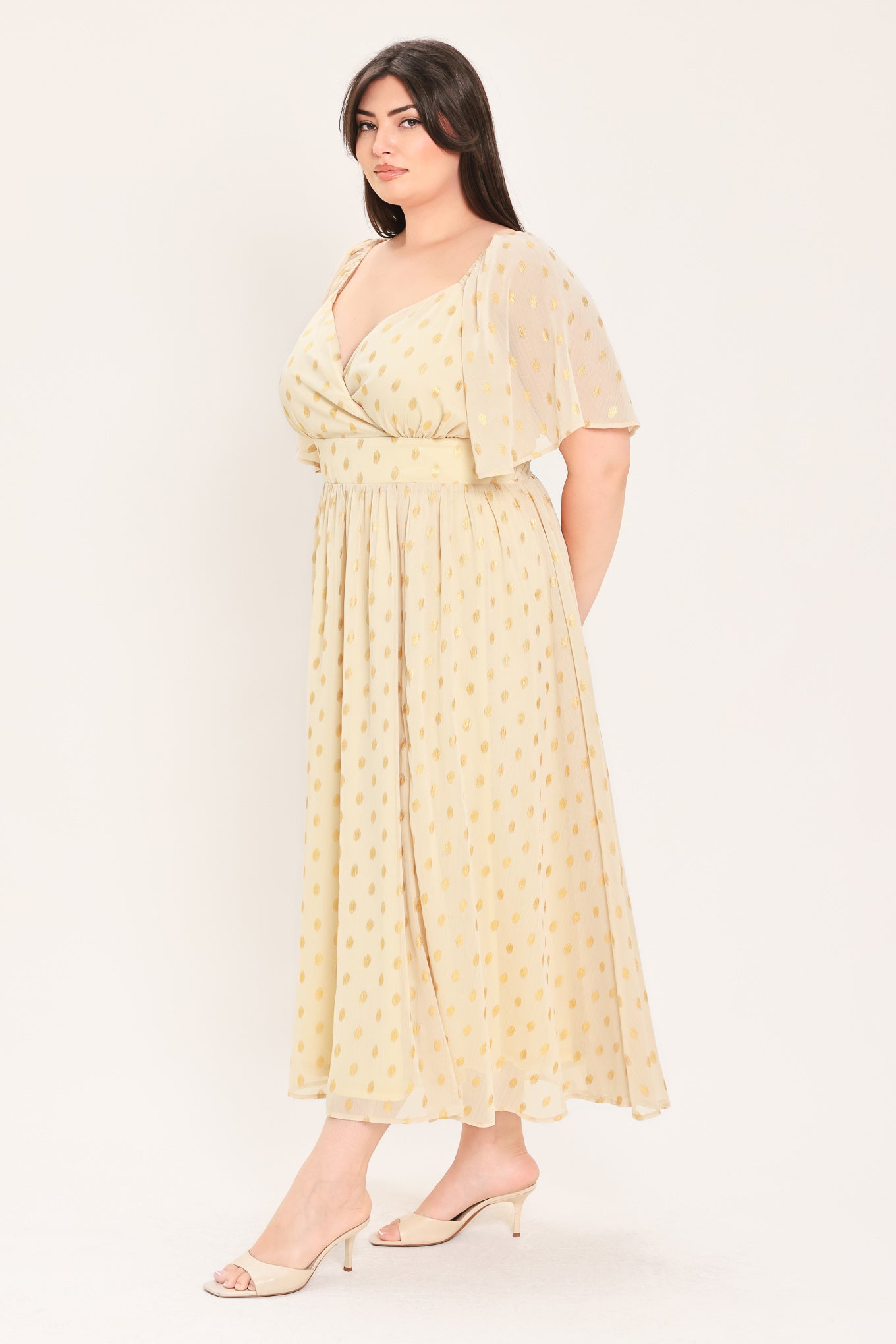 A woman modeling a light yellow midi dress with a small gold dotted pattern, featuring flutter sleeves and a V-neckline | Flying Tomato Curve
