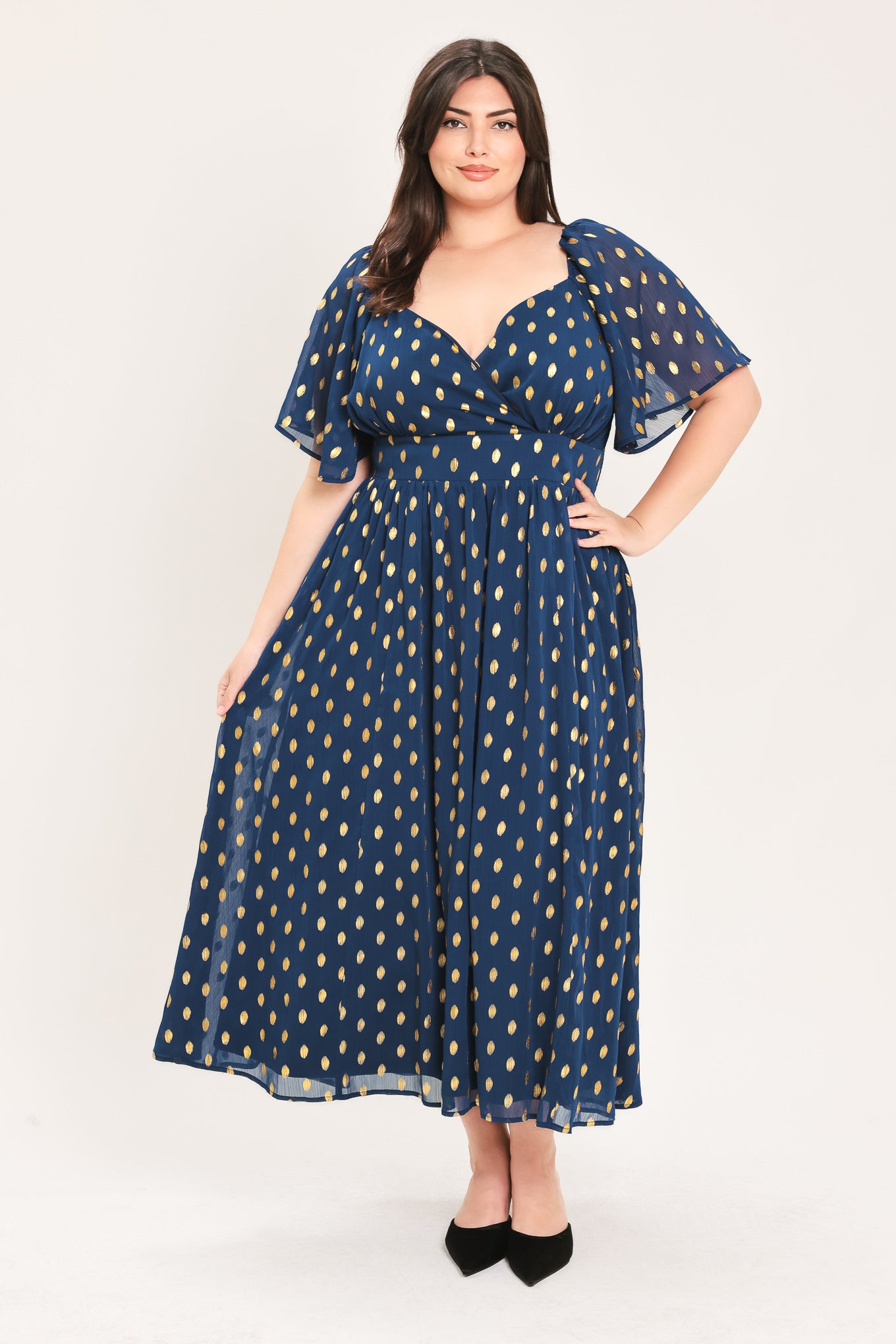 A woman modeling a light yellow midi dress with a small gold dotted pattern, featuring flutter sleeves and a V-neckline | Flying Tomato Curve