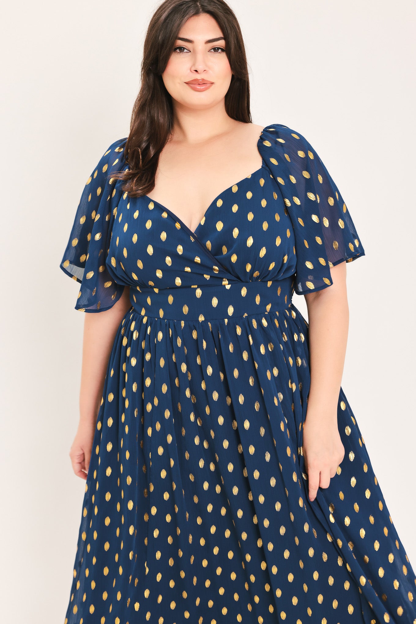 A woman modeling a light yellow midi dress with a small gold dotted pattern, featuring flutter sleeves and a V-neckline | Flying Tomato Curve