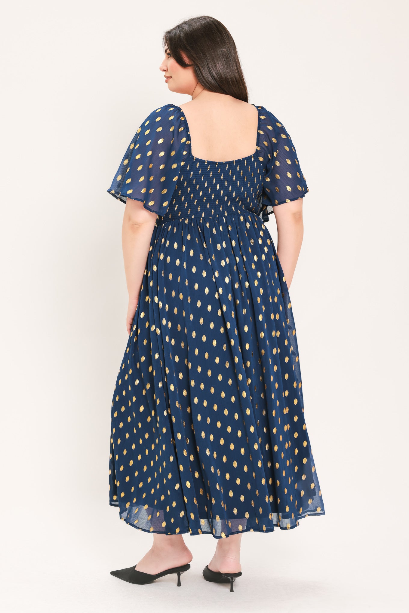A woman modeling a light yellow midi dress with a small gold dotted pattern, featuring flutter sleeves and a V-neckline | Flying Tomato Curve