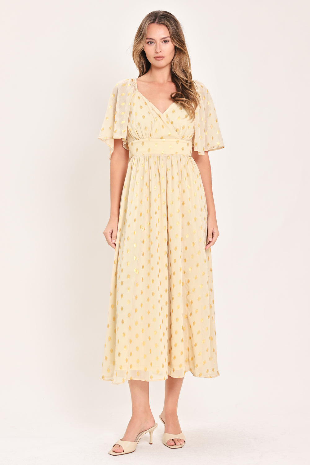 A woman modeling a light yellow midi dress with a small gold dotted pattern, featuring flutter sleeves and a V-neckline | Flying Tomato