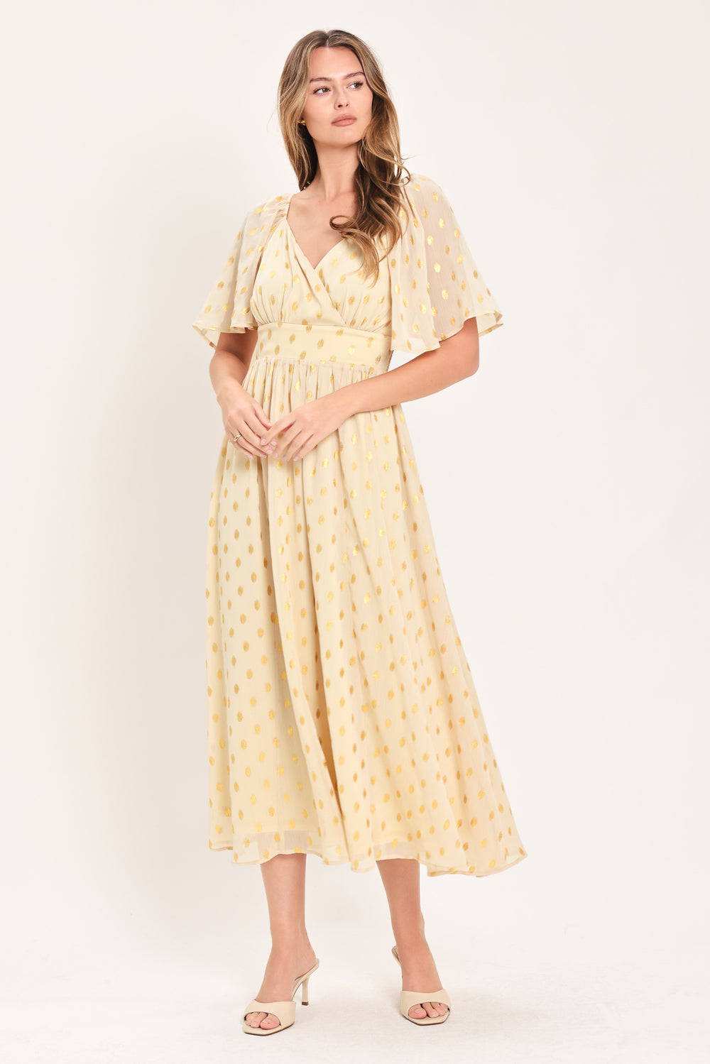 A woman modeling a light yellow midi dress with a small gold dotted pattern, featuring flutter sleeves and a V-neckline | Flying Tomato