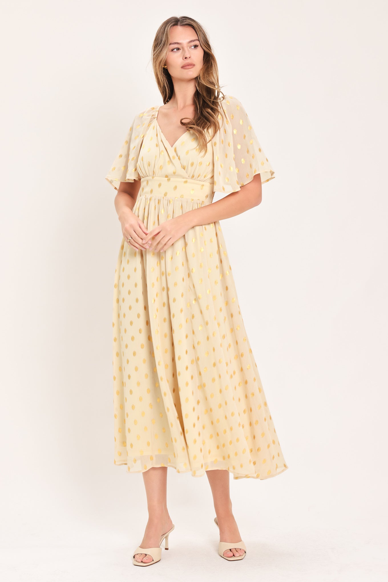 A woman modeling a light yellow midi dress with a small gold dotted pattern, featuring flutter sleeves and a V-neckline | Flying Tomato