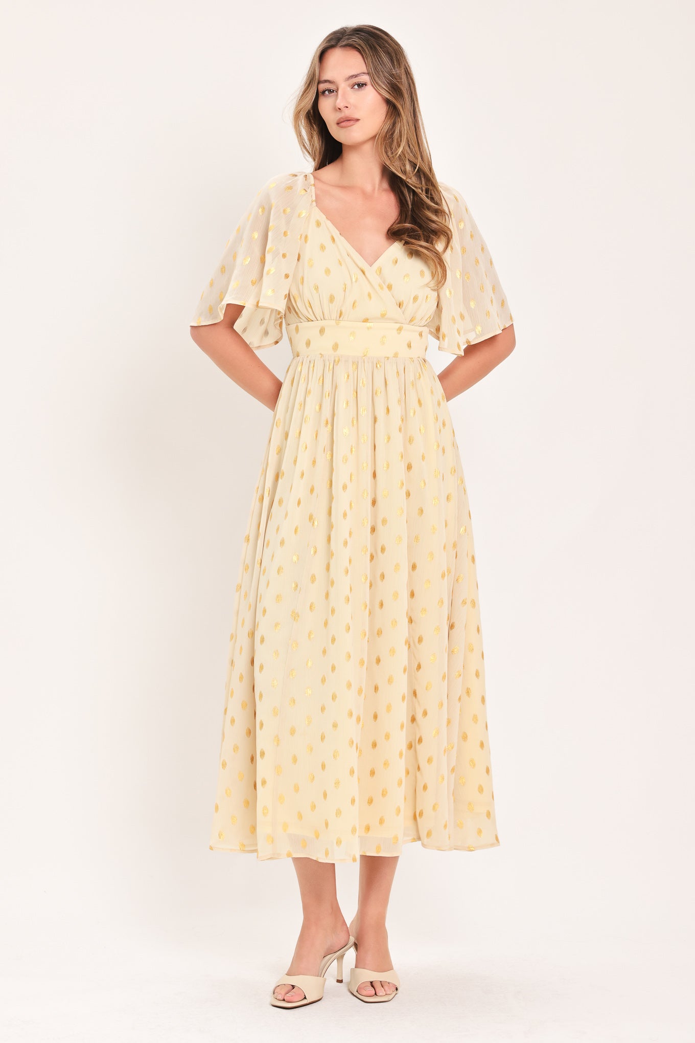 A woman modeling a light yellow midi dress with a small gold dotted pattern, featuring flutter sleeves and a V-neckline | Flying Tomato