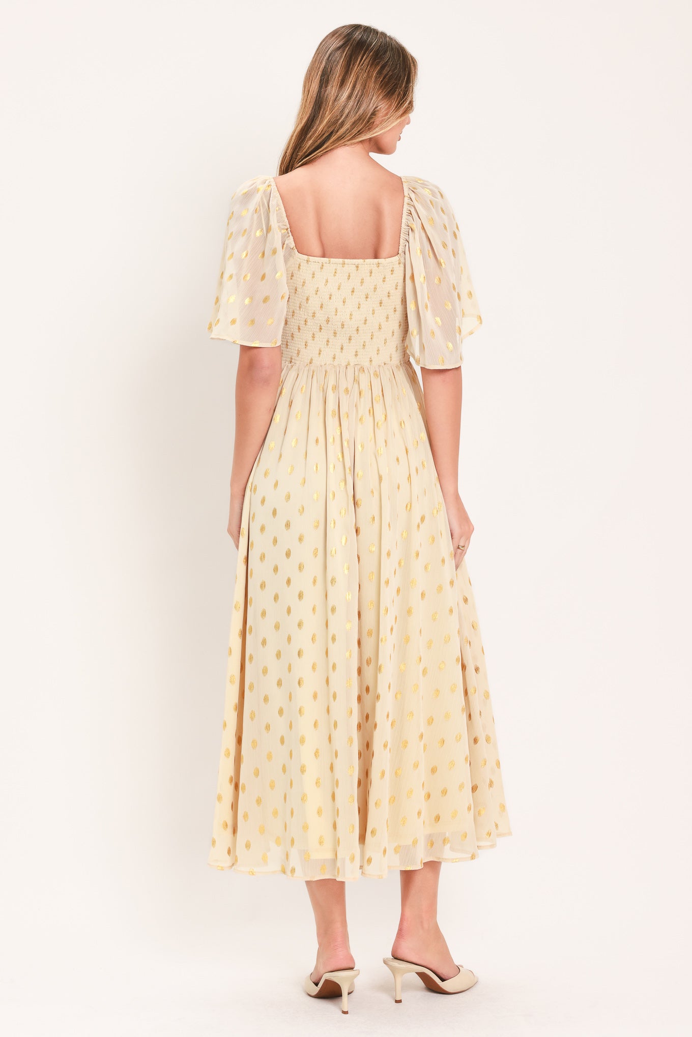 A woman modeling a light yellow midi dress with a small gold dotted pattern, featuring flutter sleeves and a V-neckline | Flying Tomato