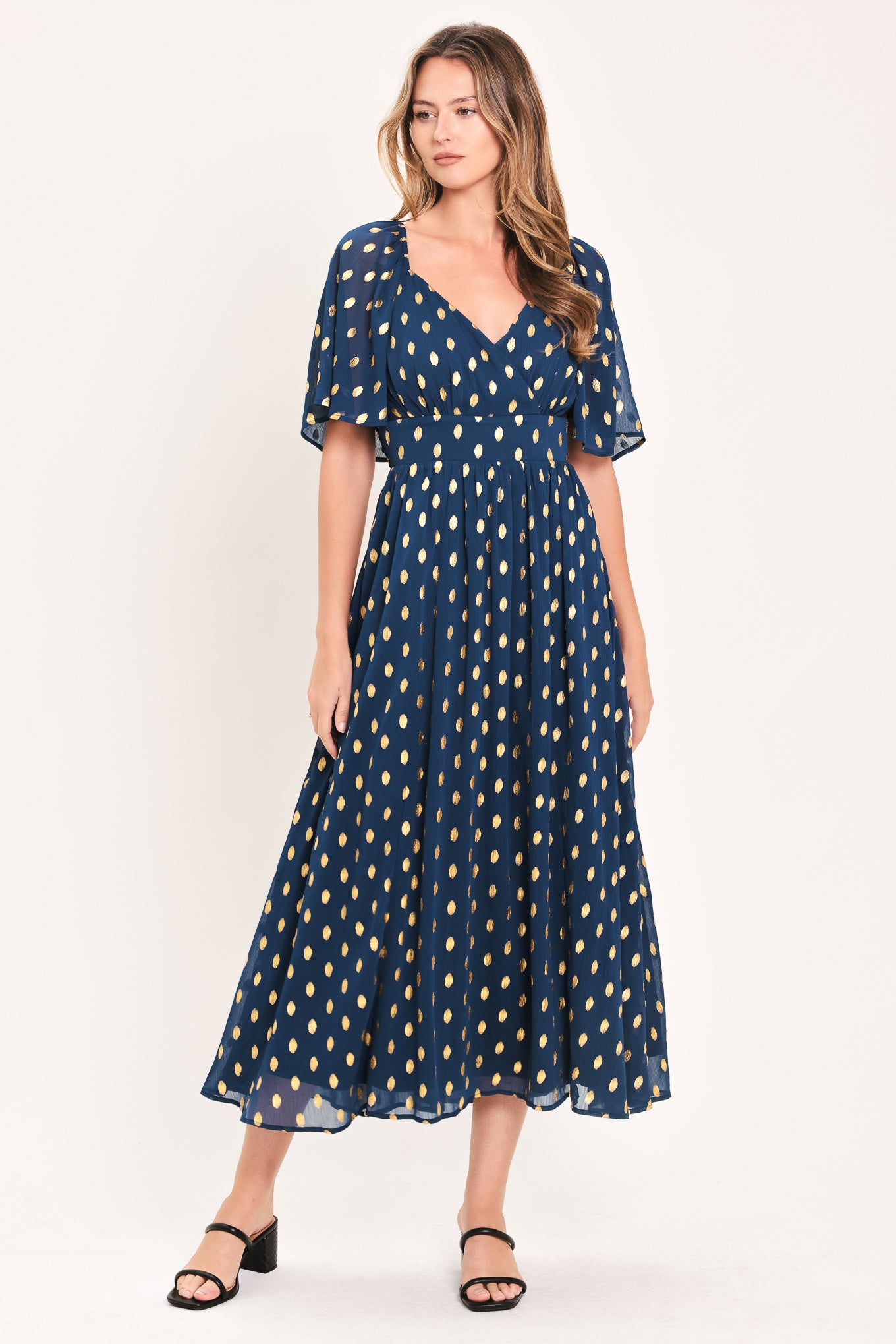 A woman modeling a navy blue midi dress with a yellow dotted pattern, featuring short flutter sleeves and a V-neckline | Flying Tomato
