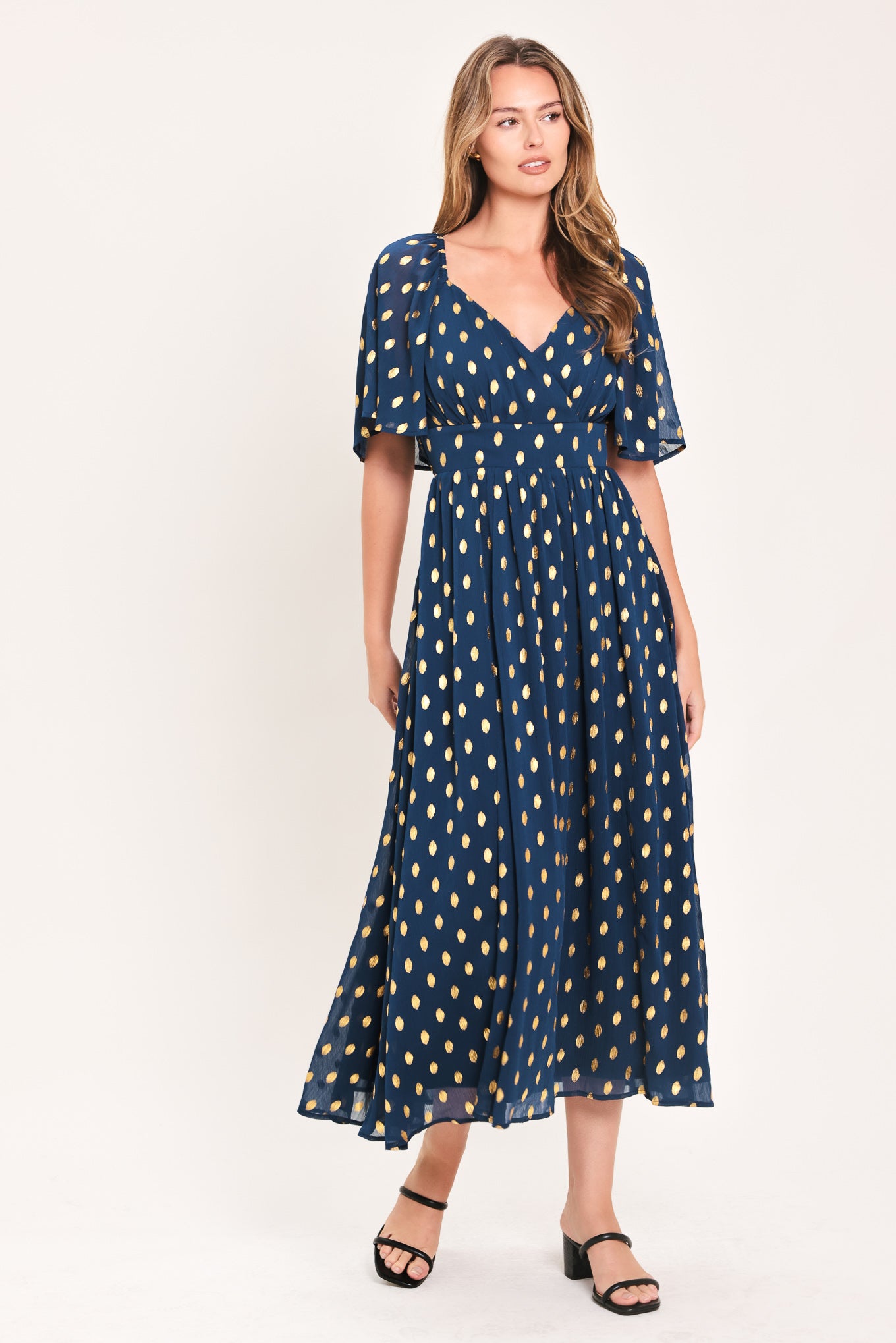 A woman modeling a light yellow midi dress with a small gold dotted pattern, featuring flutter sleeves and a V-neckline | Flying Tomato