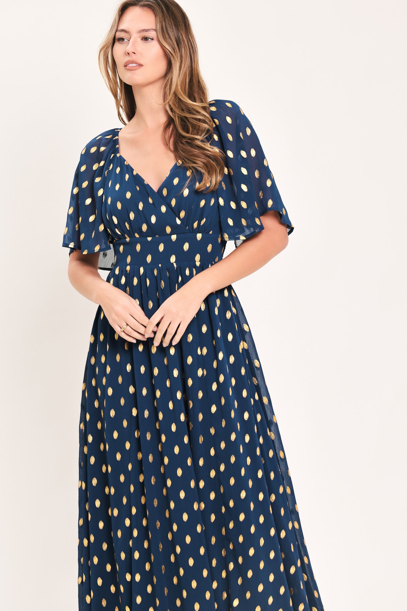 A woman modeling a light yellow midi dress with a small gold dotted pattern, featuring flutter sleeves and a V-neckline | Flying Tomato