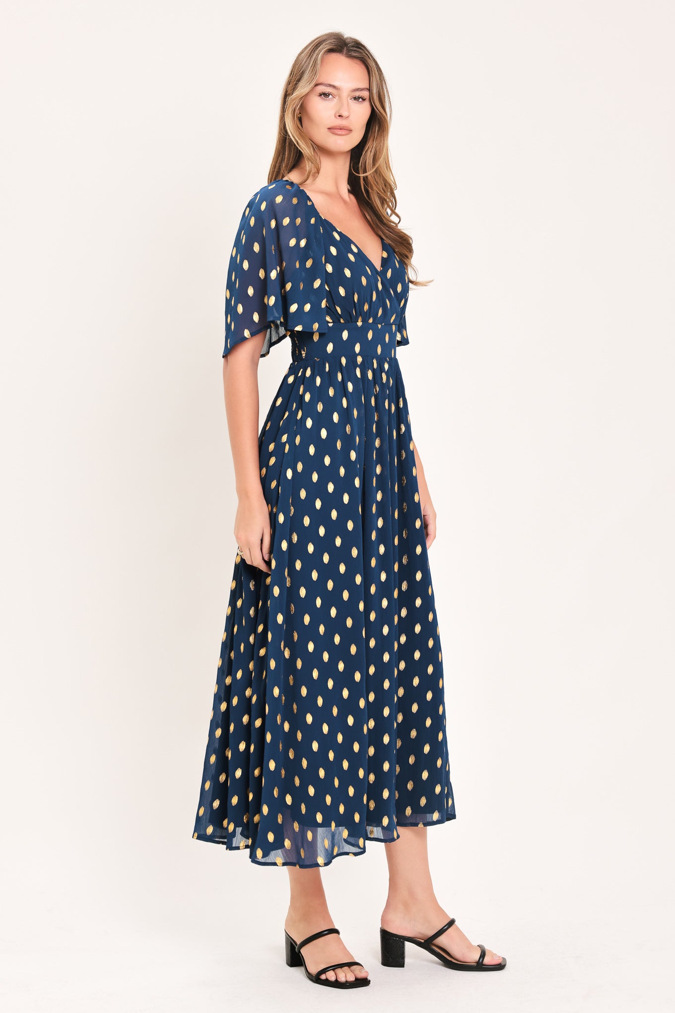 A woman modeling a light yellow midi dress with a small gold dotted pattern, featuring flutter sleeves and a V-neckline | Flying Tomato