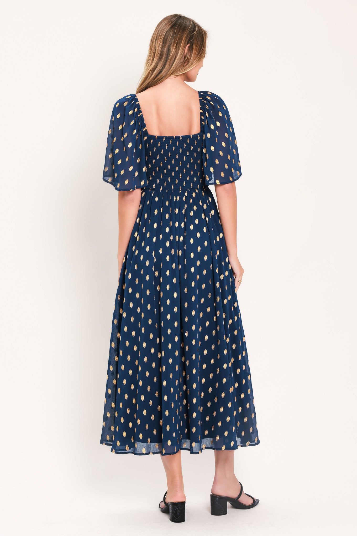 A woman modeling a light yellow midi dress with a small gold dotted pattern, featuring flutter sleeves and a V-neckline | Flying Tomato