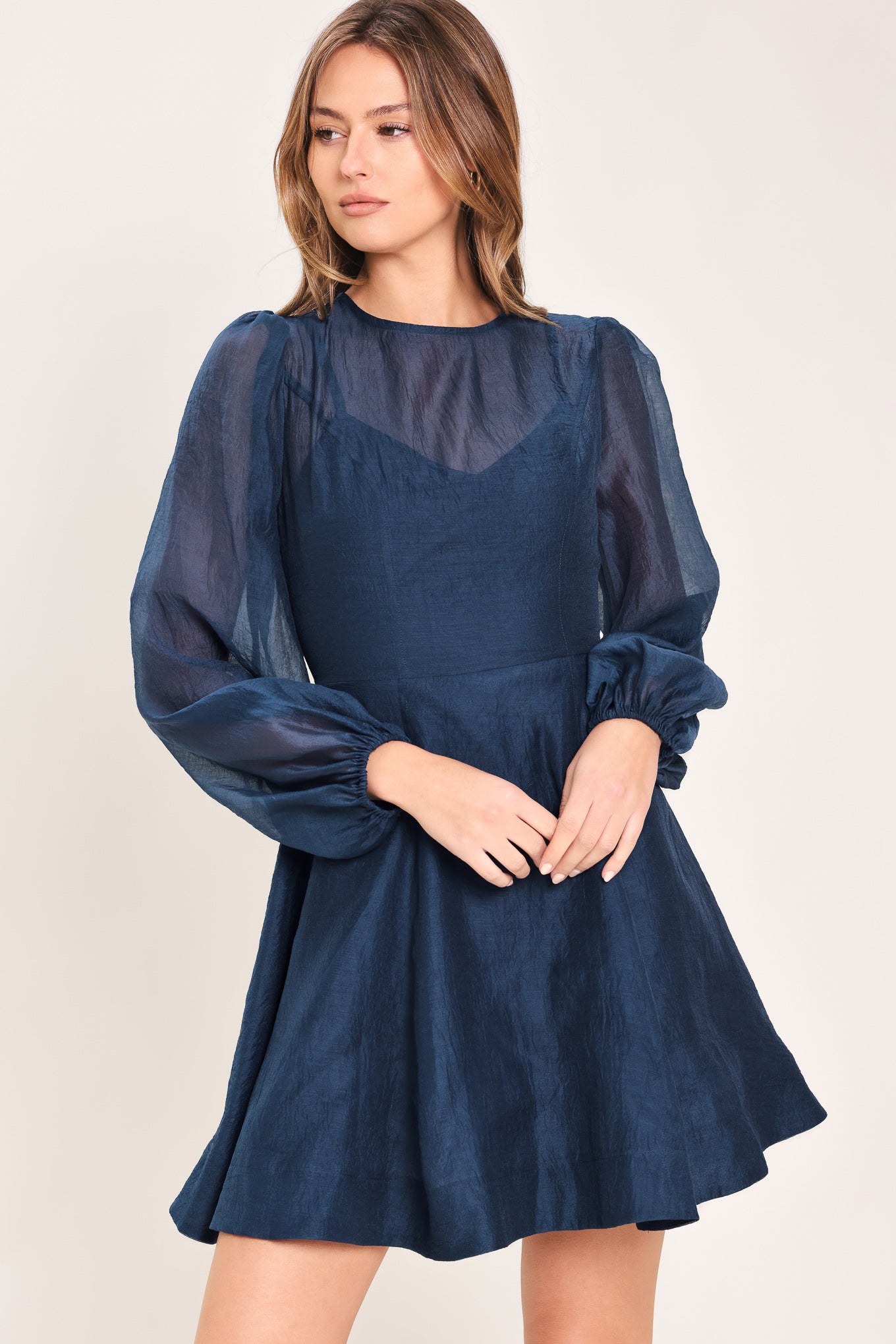 Woman wearing a blue mini dress with sheer long sleeves featuring round neckline, long sleeve, circle skirt and back zipper closure | Flying Tomato
