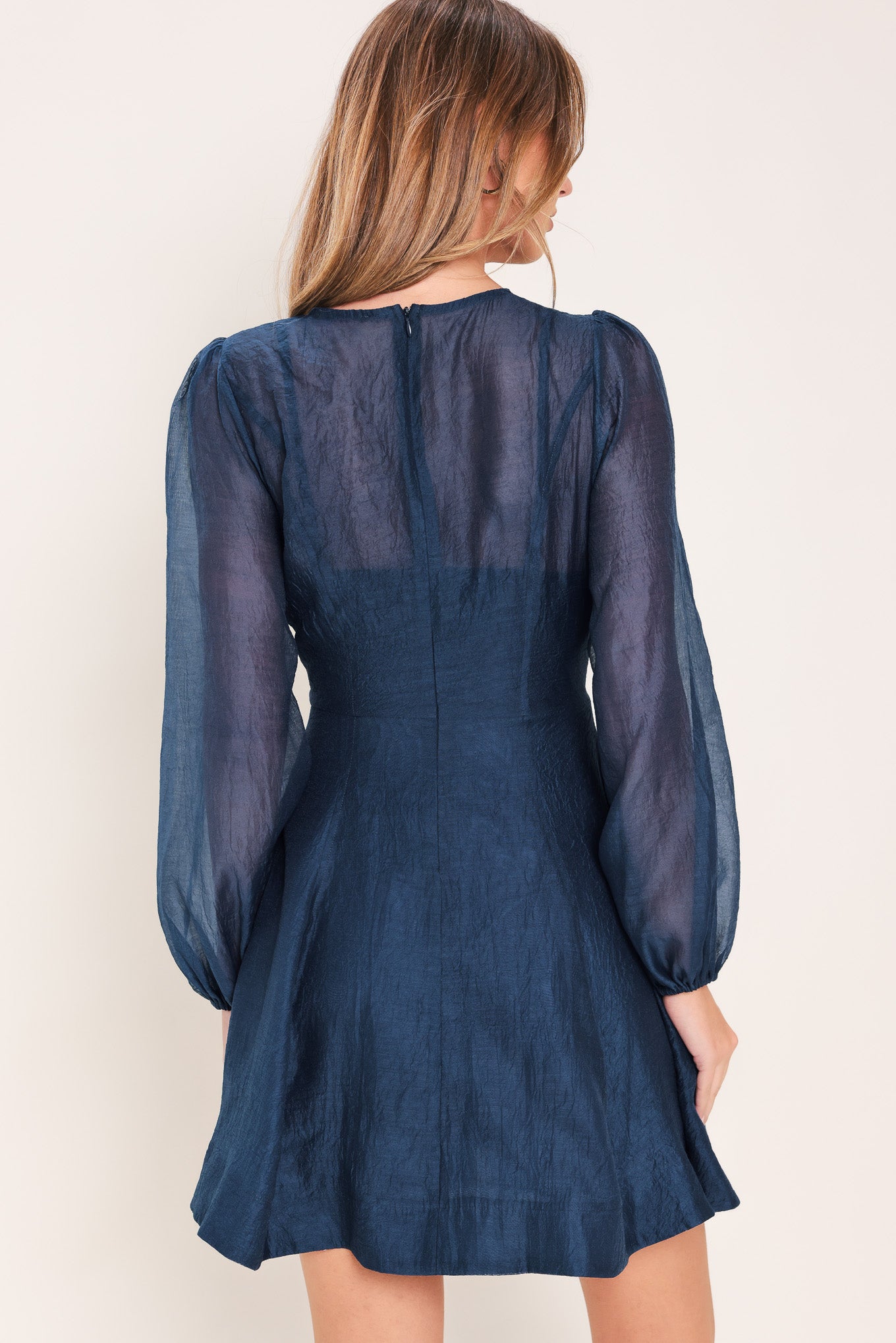 Woman wearing a blue mini dress with sheer long sleeves featuring round neckline, long sleeve, circle skirt and back zipper closure | Flying Tomato