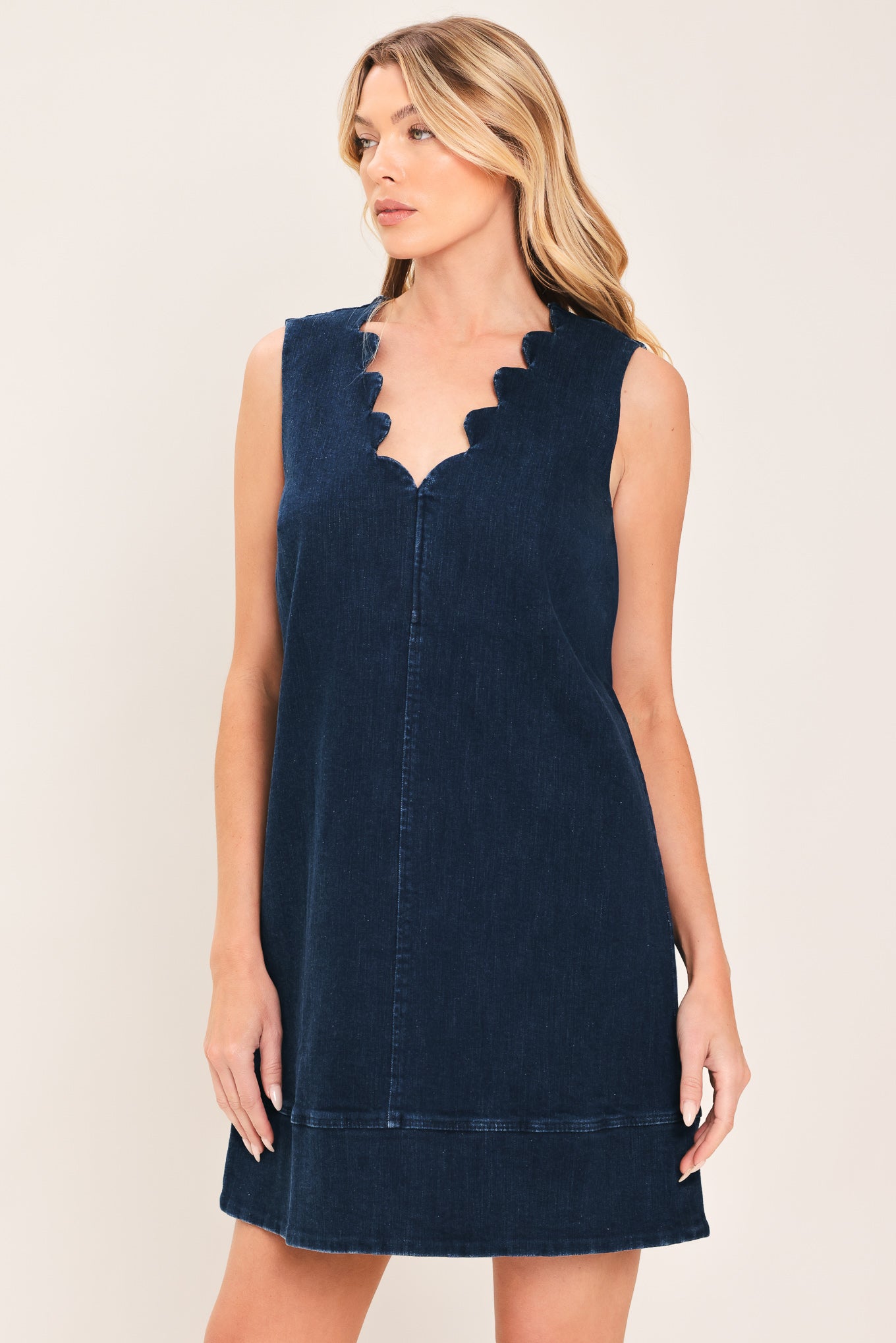 A woman wearing a sleeveless dark navy blue dress with a scalloped V-neckline | Flying Tomato