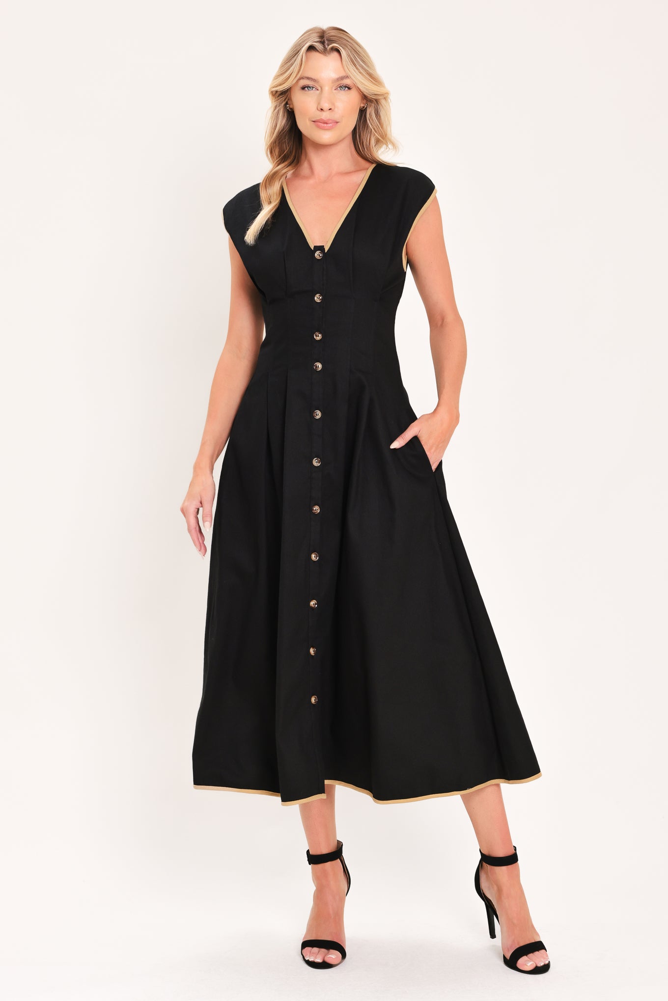 A woman modeling a sleeveless black midi dress with a V-neckline, front button placket, side pockets, and thin gold trim at the hem | Flying Tomato