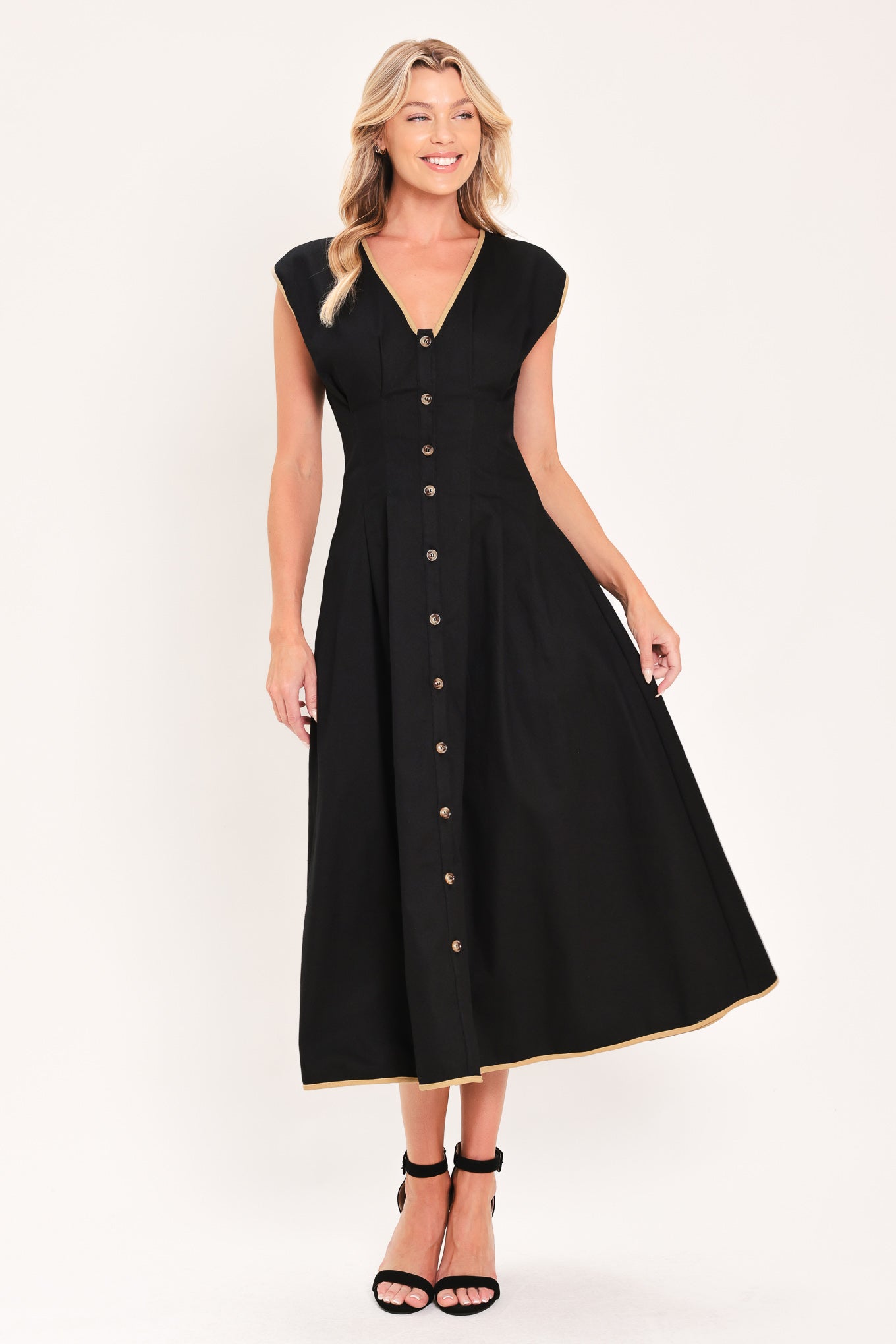 A woman modeling a sleeveless black midi dress with a V-neckline, front button placket, side pockets, and thin gold trim at the hem | Flying Tomato