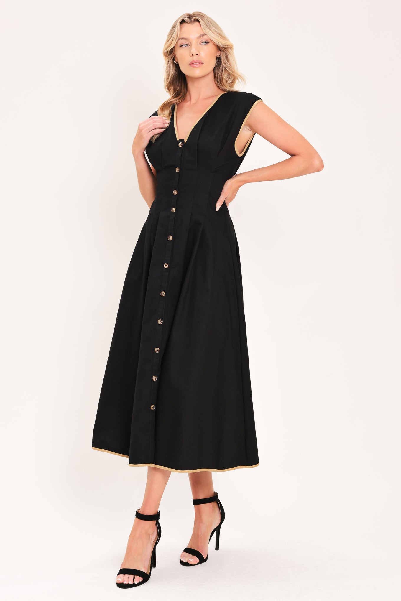 A woman modeling a sleeveless black midi dress with a V-neckline, front button placket, side pockets, and thin gold trim at the hem | Flying Tomato
