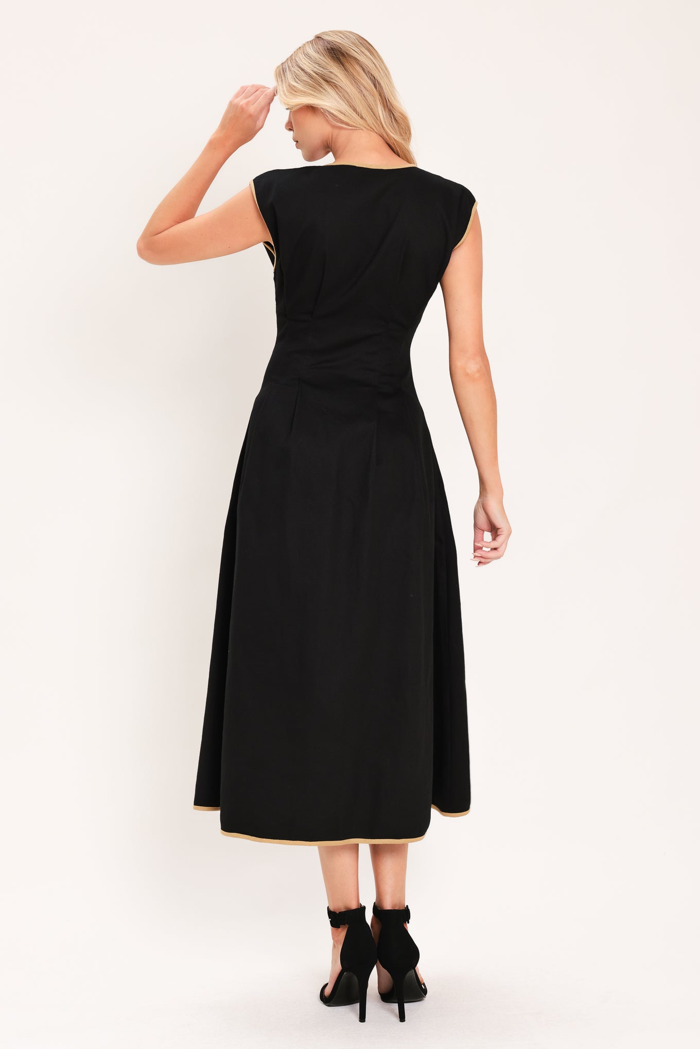 A woman modeling a sleeveless black midi dress with a V-neckline, front button placket, side pockets, and thin gold trim at the hem | Flying Tomato