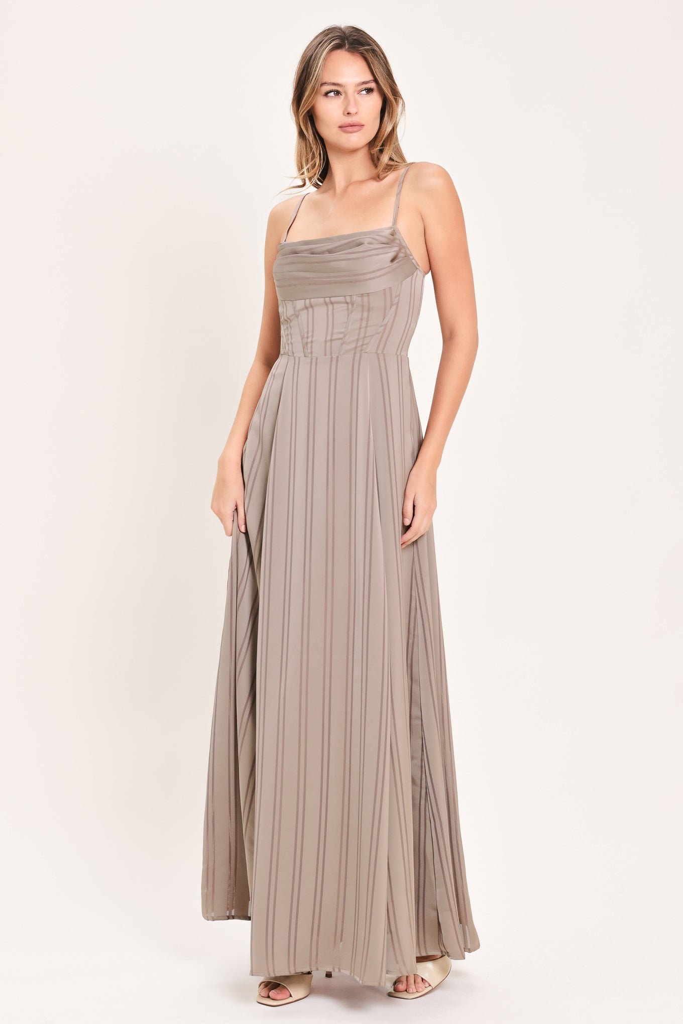 A woman modeling a floor-length taupe pleated maxi dress with spaghetti straps and a gathered sweetheart neckline | Flying Tomato