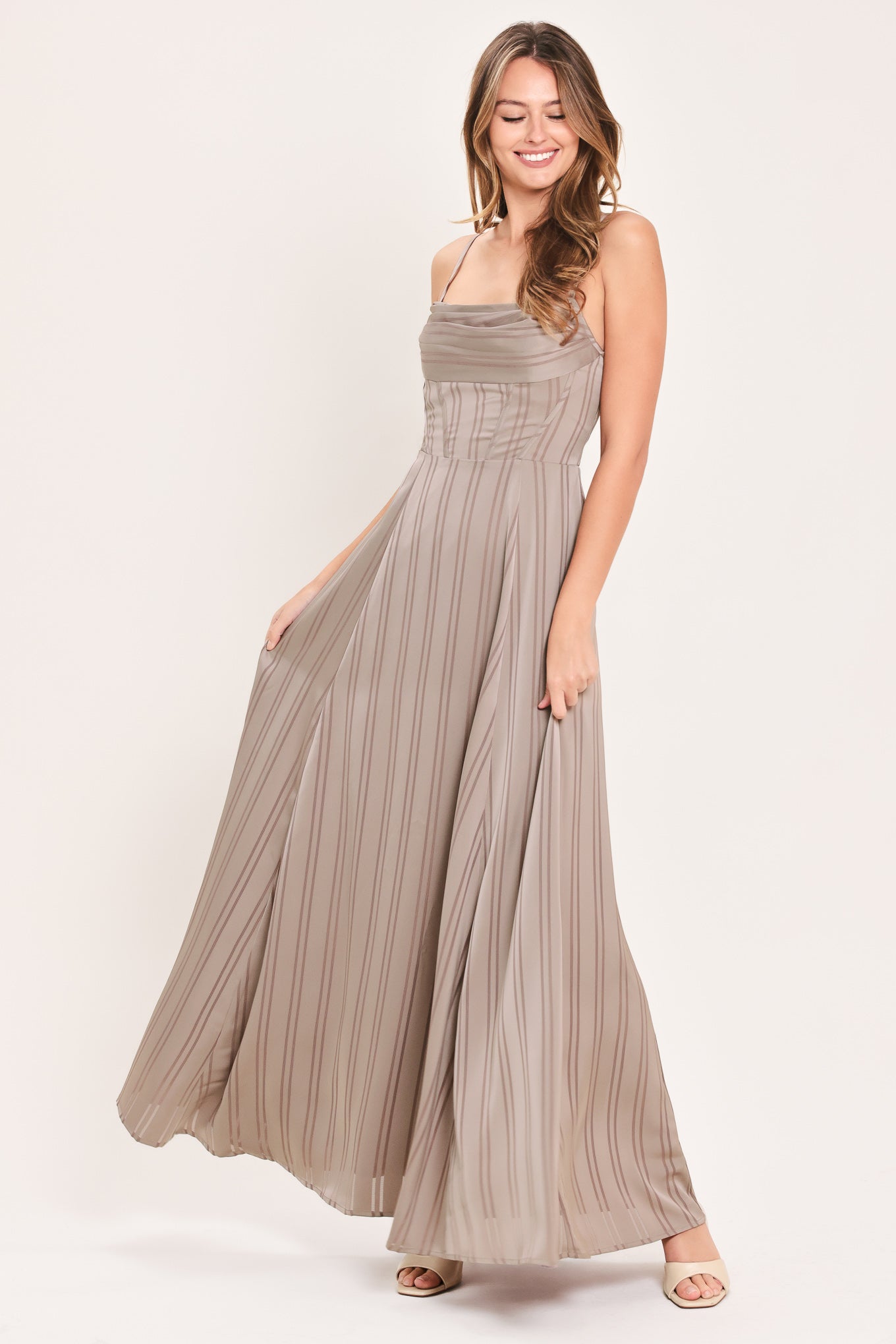 A woman modeling a floor-length taupe pleated maxi dress with spaghetti straps and a gathered sweetheart neckline | Flying Tomato