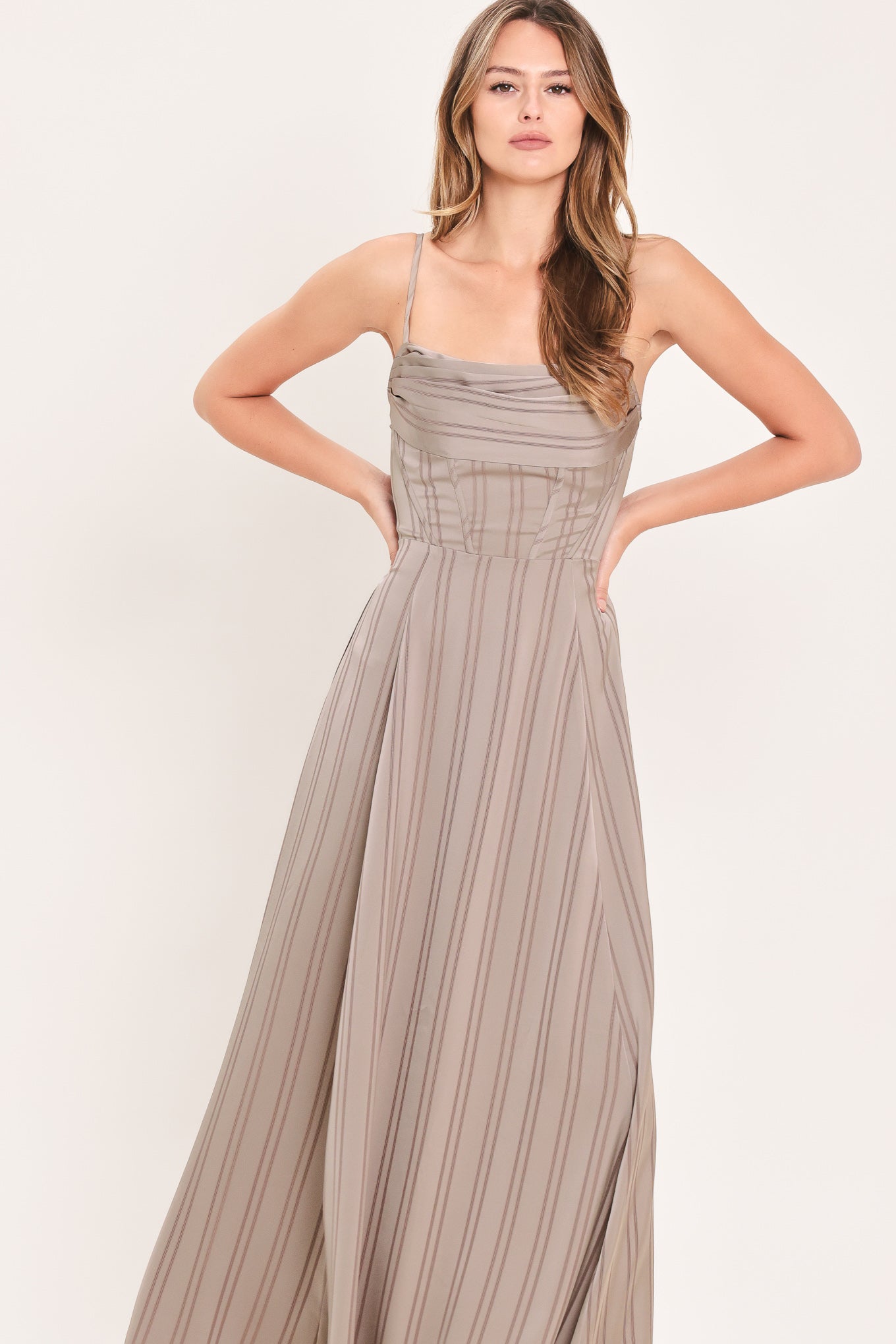 A woman modeling a floor-length taupe pleated maxi dress with spaghetti straps and a gathered sweetheart neckline | Flying Tomato