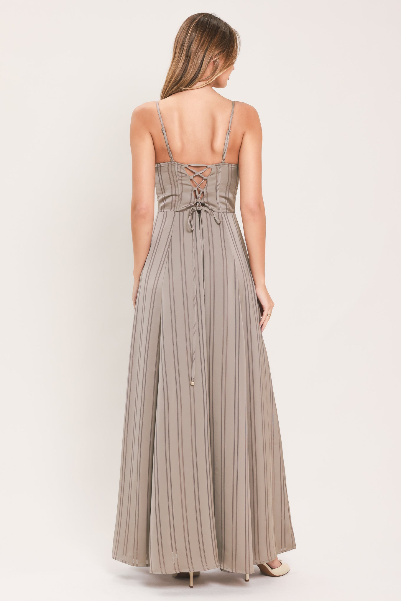 A woman modeling a floor-length taupe pleated maxi dress with spaghetti straps and a gathered sweetheart neckline | Flying Tomato