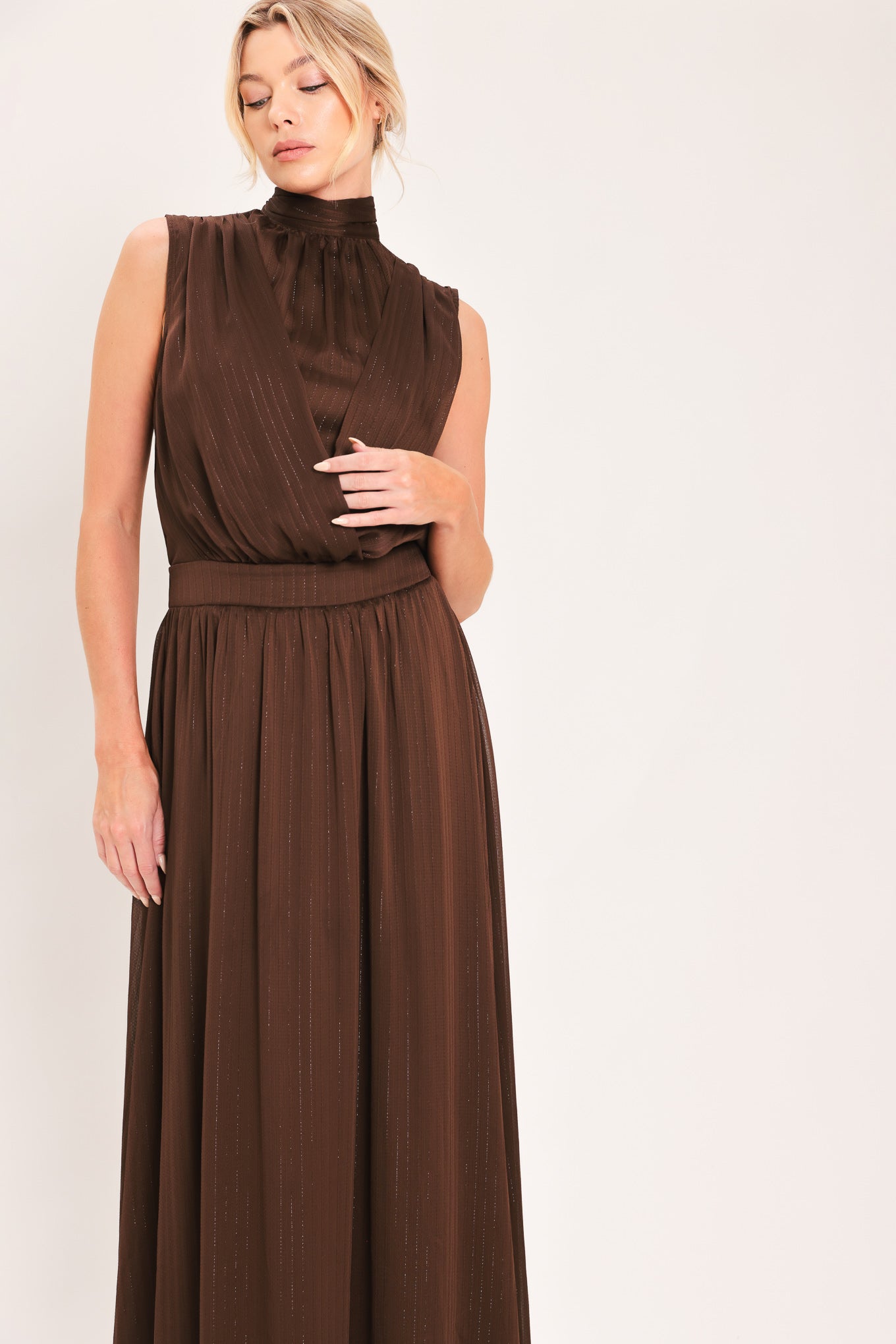 A woman modeling a sleeveless, high-neck, maxi brown dress | Flying Tomato