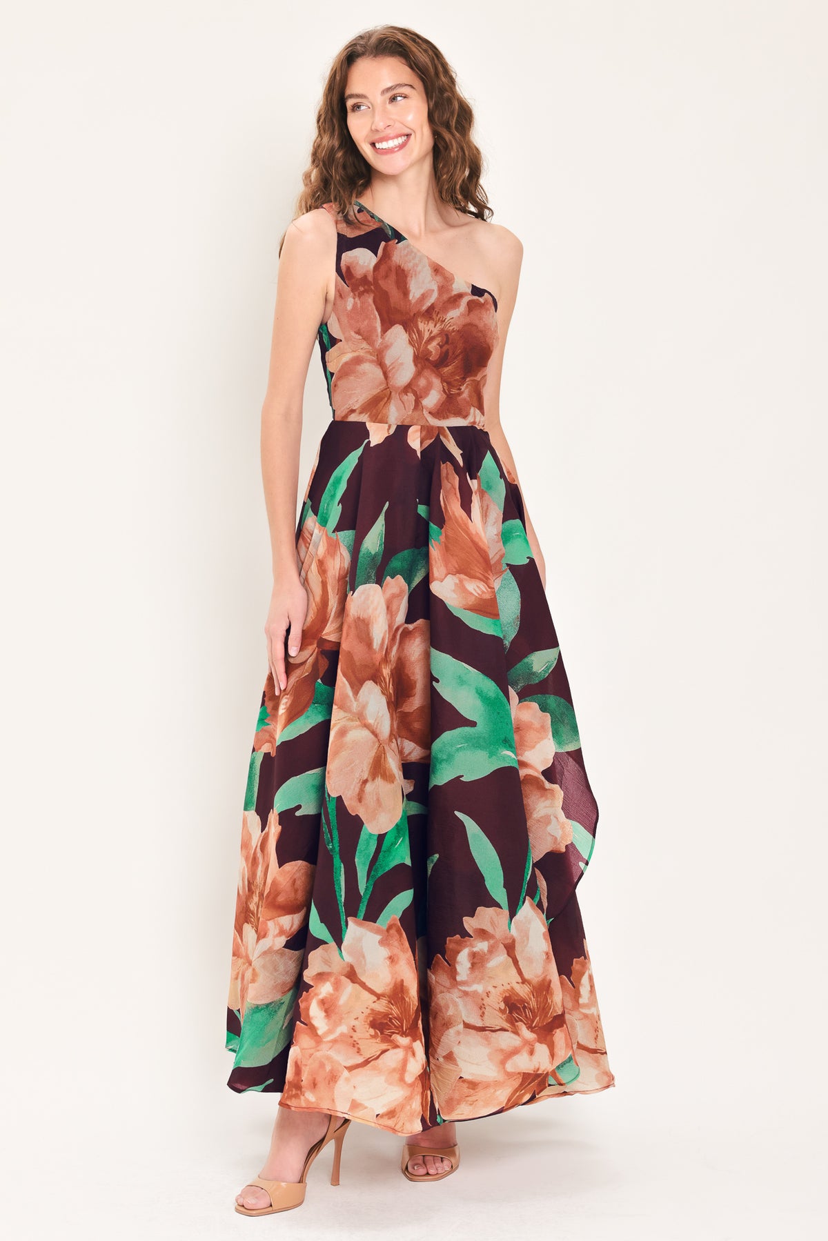 A woman modeling a one-shoulder wine-colored maxi dress with a large floral print in peach, brown, and green | Flying Tomato