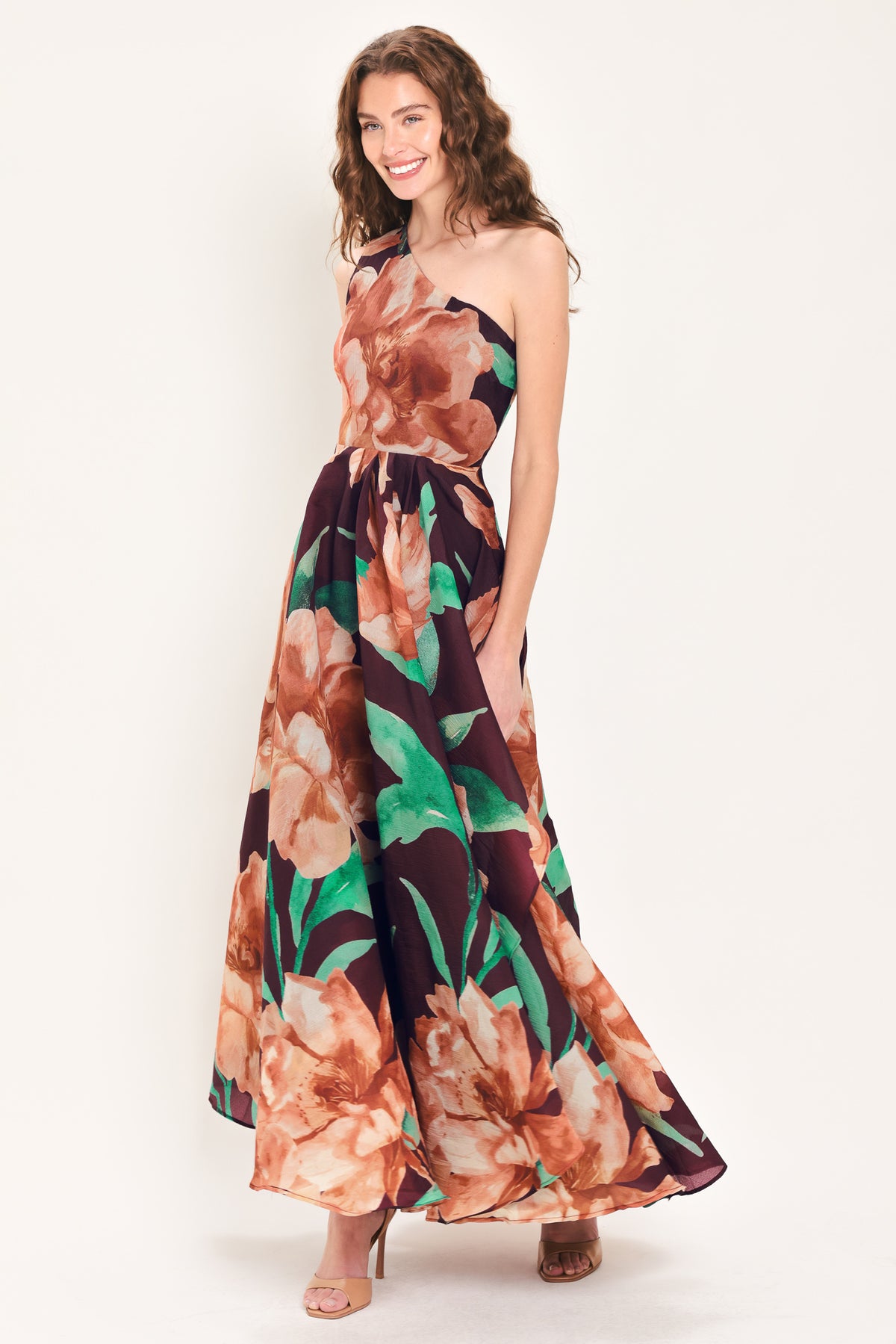 A woman modeling a one-shoulder wine-colored maxi dress with a large floral print in peach, brown, and green | Flying Tomato