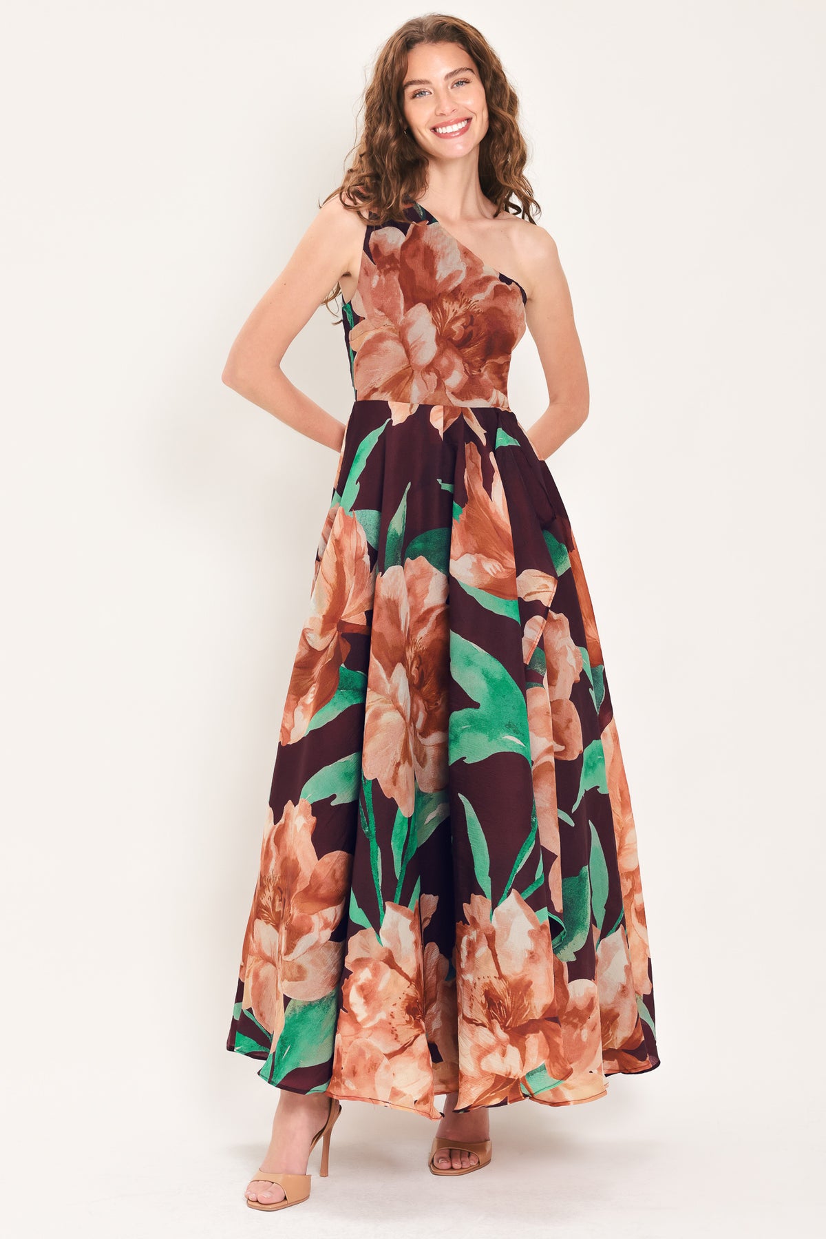 A woman modeling a one-shoulder wine-colored maxi dress with a large floral print in peach, brown, and green | Flying Tomato